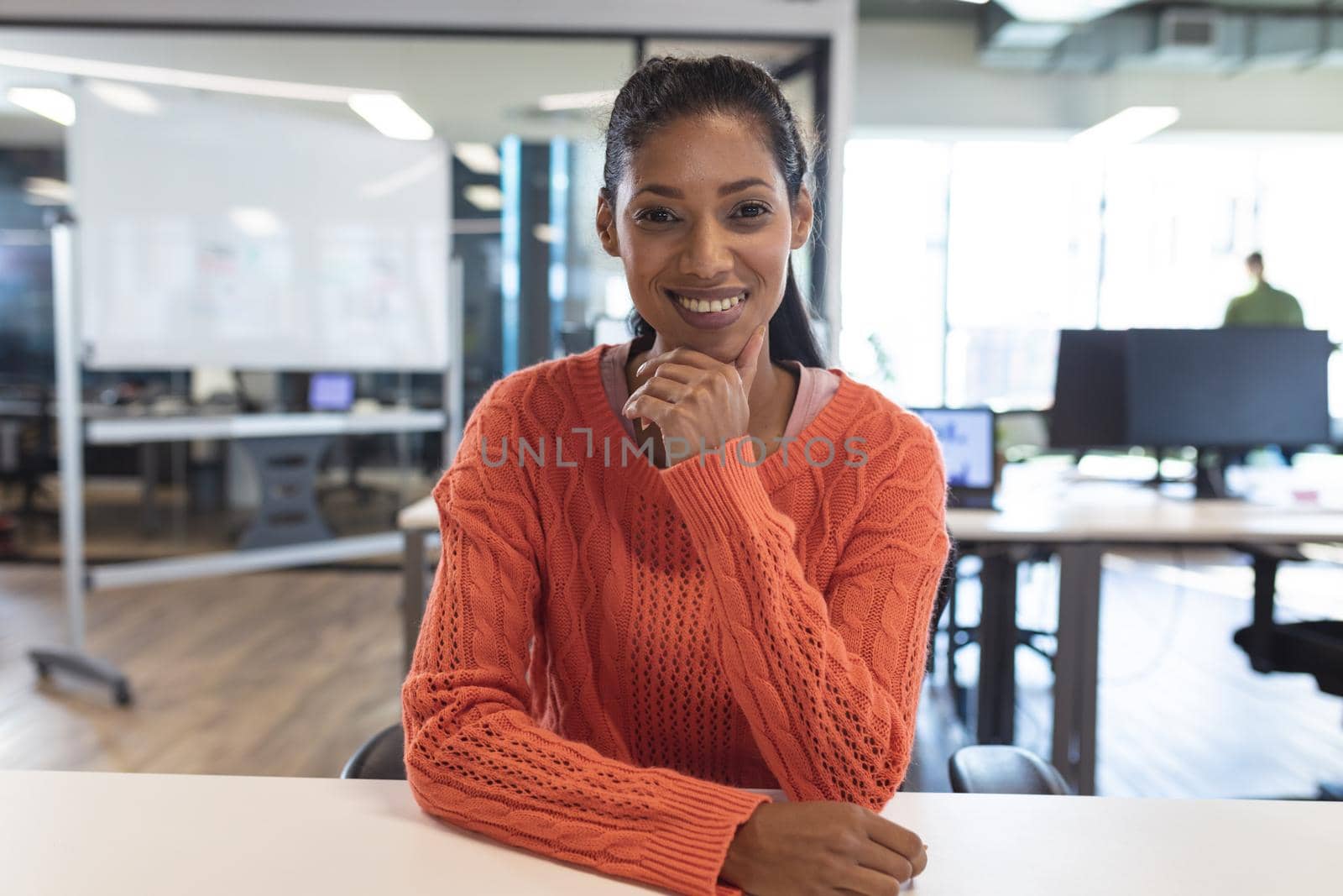 Portrait of mixed race female creative worker sitting at desk looking at camera. modern office of a creative design business.