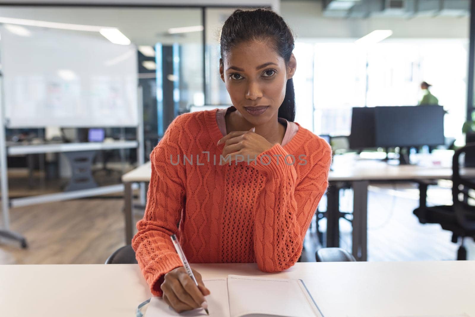 Portrait of mixed race female creative worker sitting at desk looking at camera by Wavebreakmedia