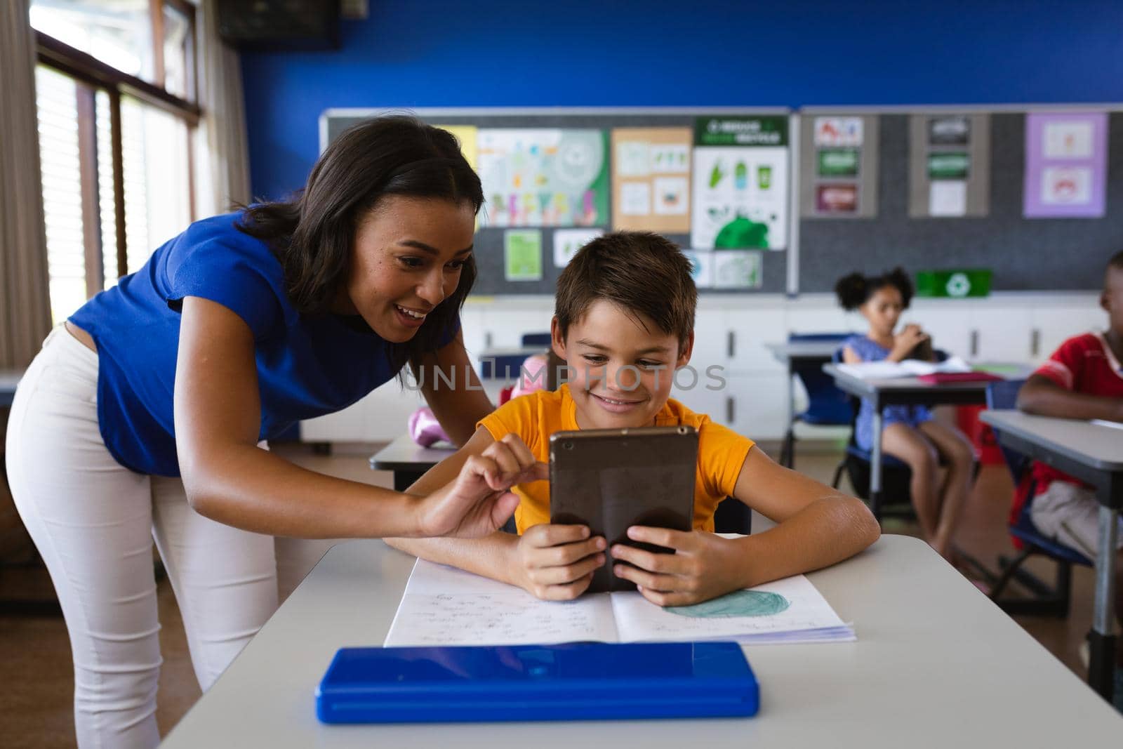 African american female teacher teaching a boy to use digital tablet in class at elementary school. education back to school health safety during covid19 coronavirus pandemic