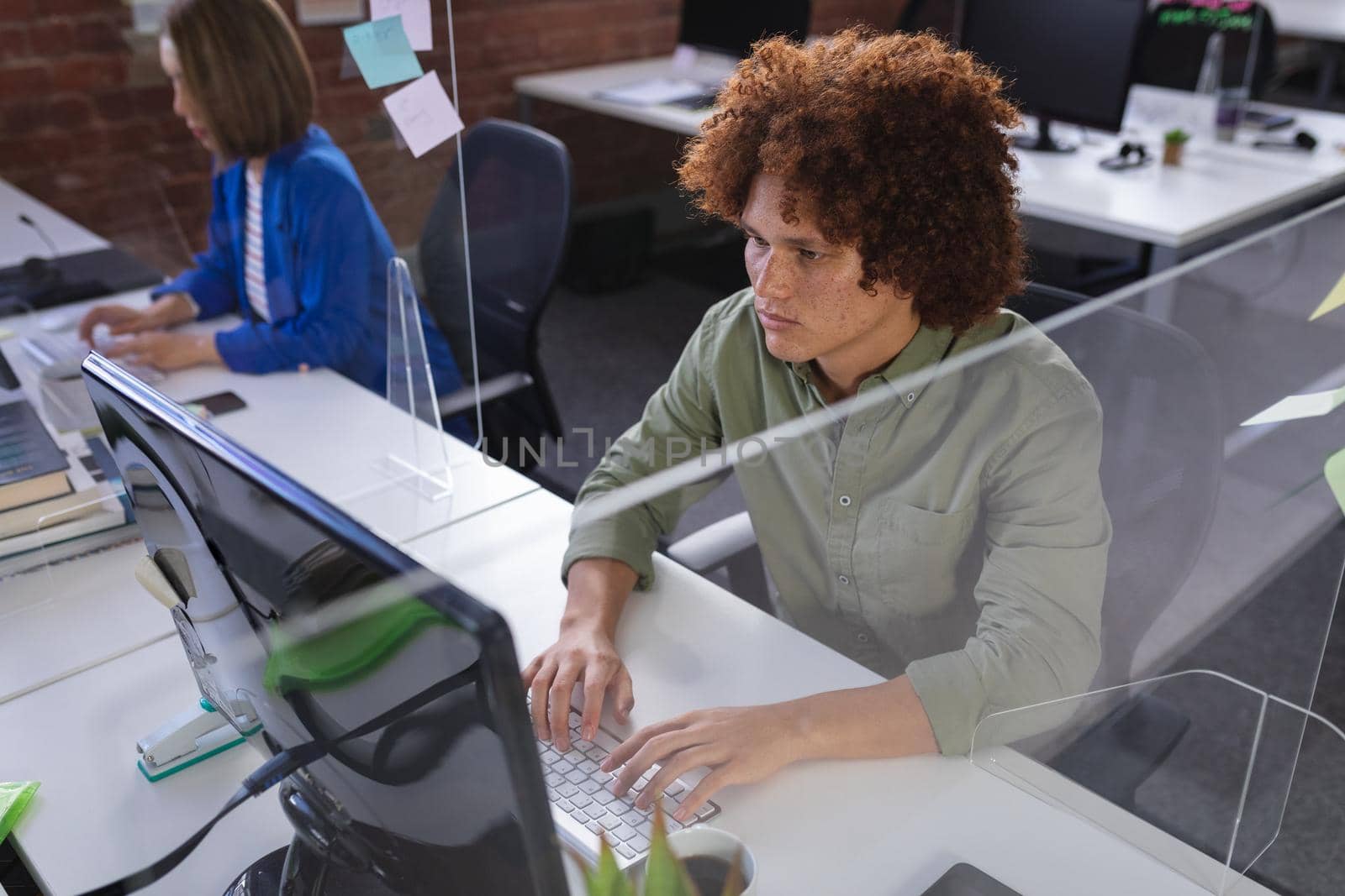 Diverse male and female colleagues sitting in front of computers separated by sneeze shields by Wavebreakmedia