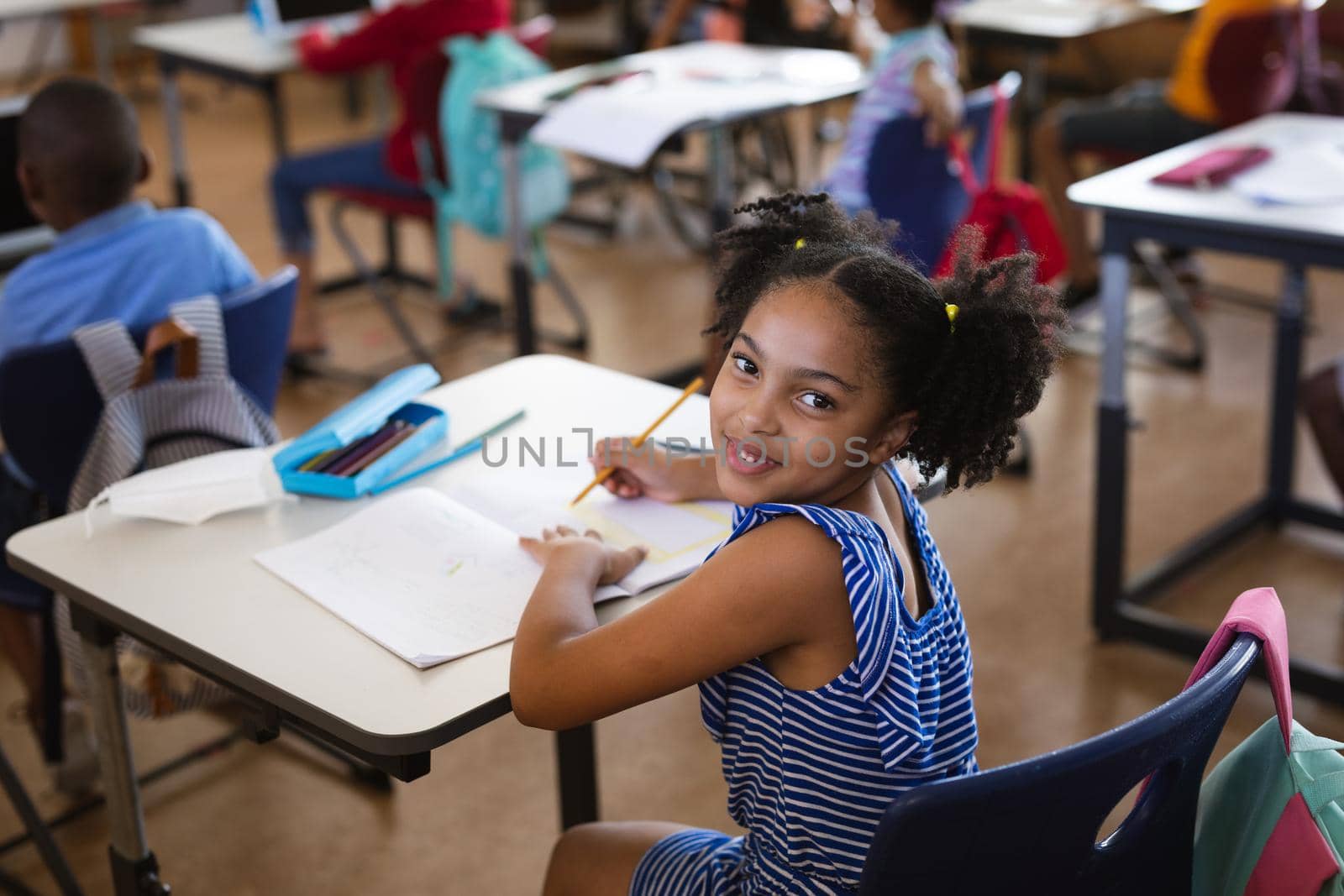 Portrait of african american girl smiling while sitting on her desk in class at elementary school. school and education concept