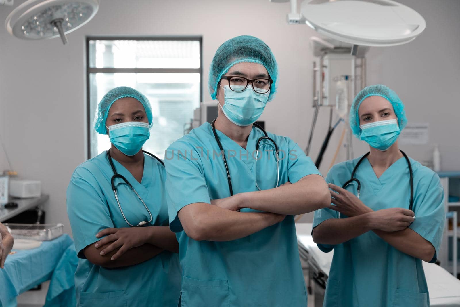 Diverse group of male and female doctors standing in operating theatre wearing face masks. medicine, health and healthcare services during coronavirus covid 19 pandemic.