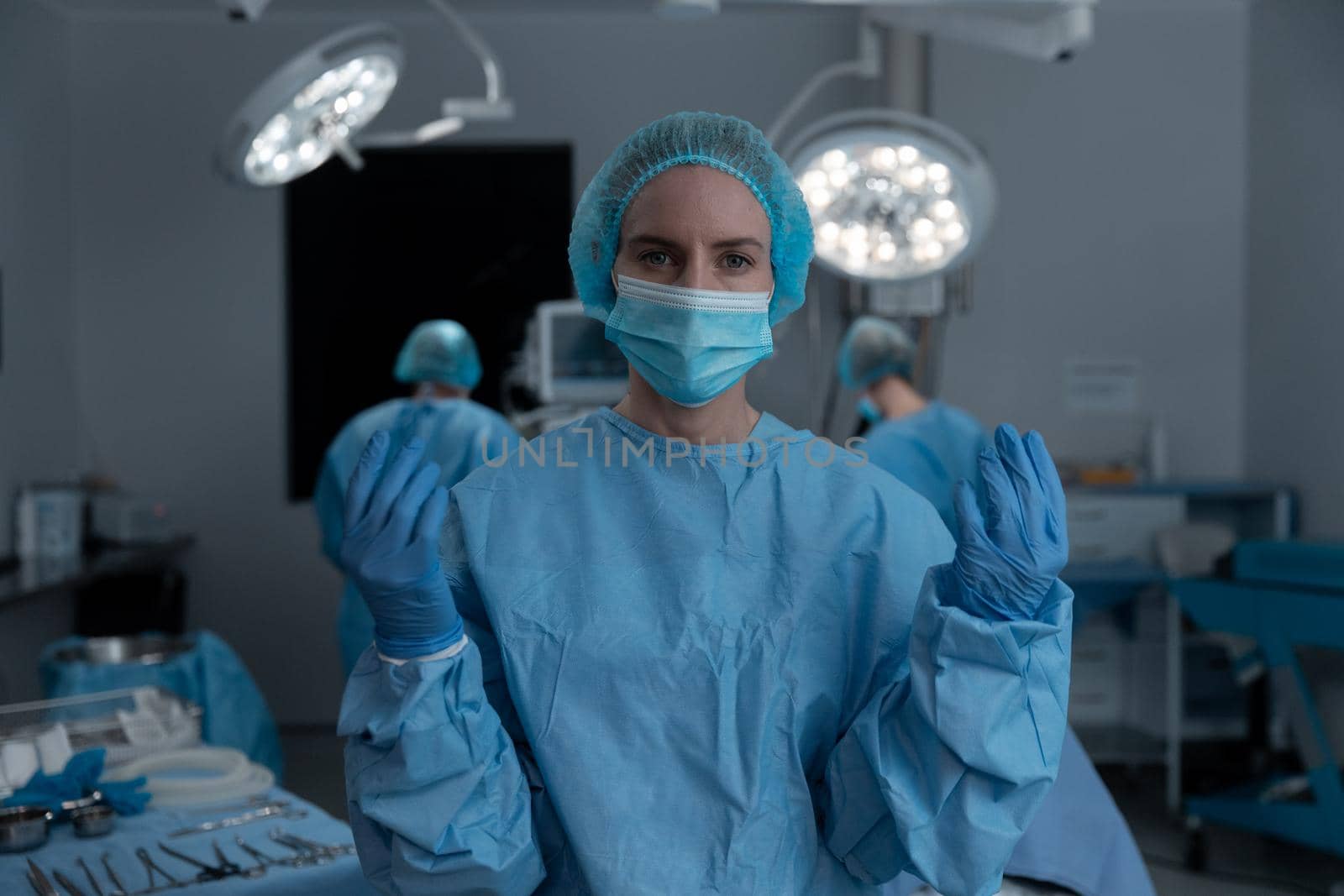 Portrait of caucasian female surgeon wearing face mask, gloves, cap and scrubs in operating theatre. medicine, health and healthcare services during covid 19 coronavirus pandemic.
