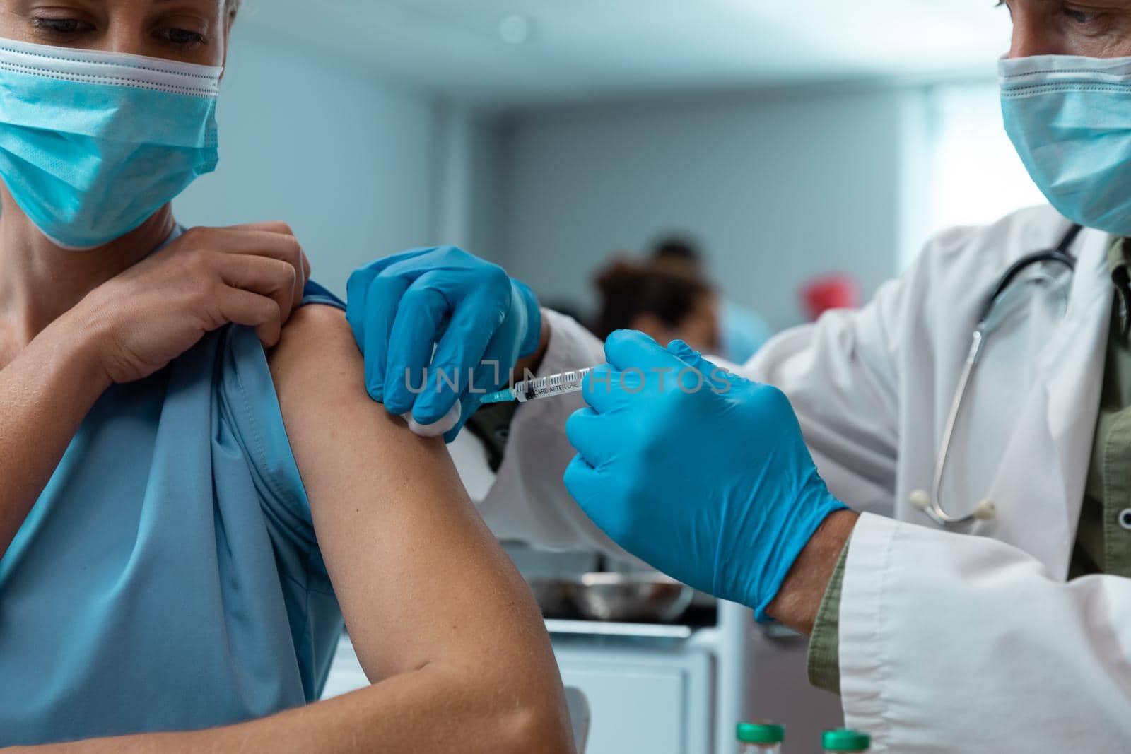 Caucasian male doctor giving covid vaccination to female colleague at hospital, both in face masks. medicine, health and healthcare services during covid 19 coronavirus pandemic.