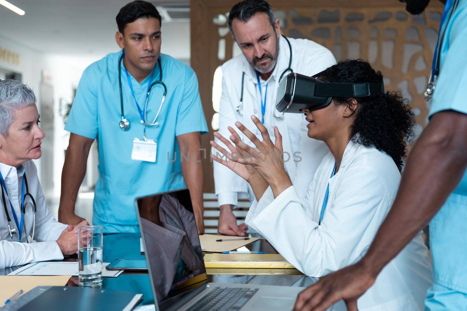 Diverse male and female doctors wearing face masks sitting at table and using vr glasses. medicine, health and healthcare services.