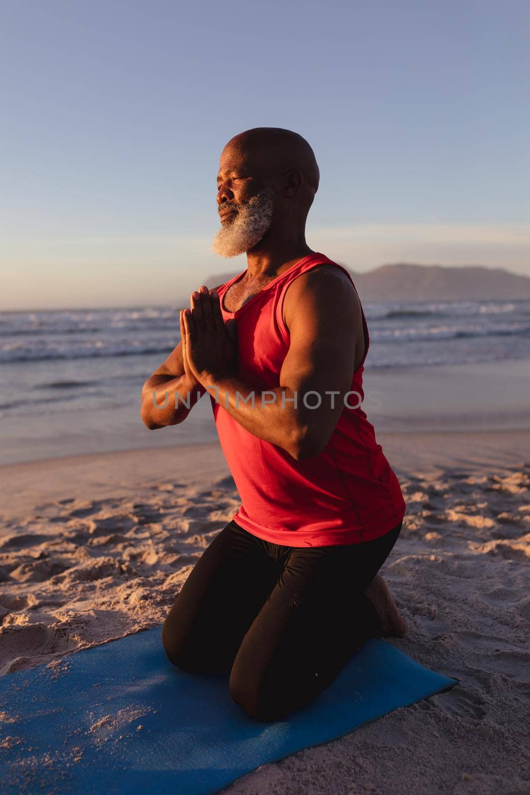 Senior african american man with folded hands meditating and practicing yoga at the beach by Wavebreakmedia