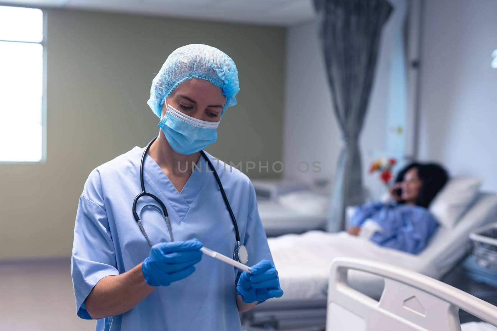 Caucasian female doctor in hospital wearing face mask and surgical gloves holding swab test. medical professional at work during coronavirus covid 19 pandemic.