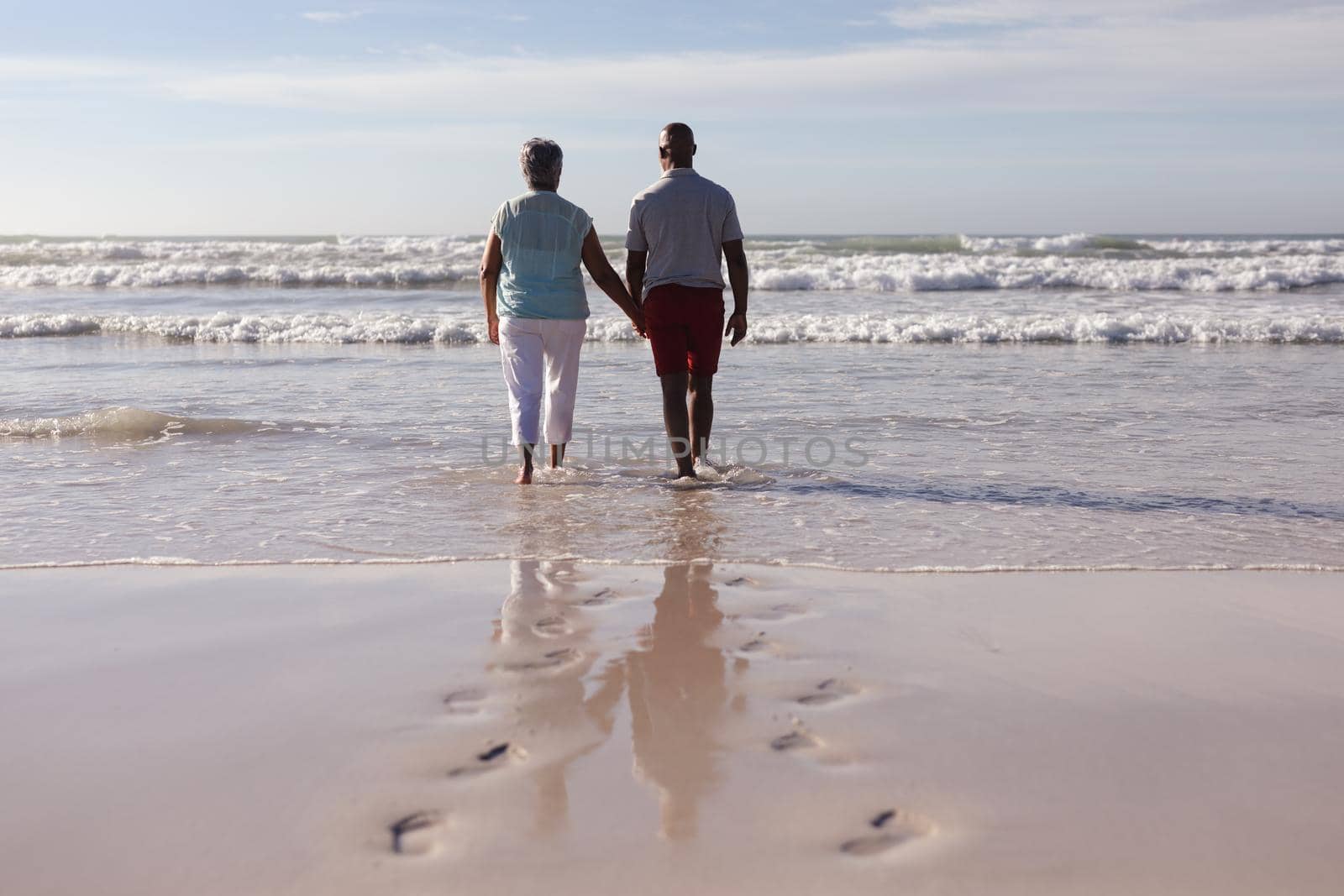 Rear view of senior african american couple holding hands while walking on the beach. travel vacation retirement lifestyle concept