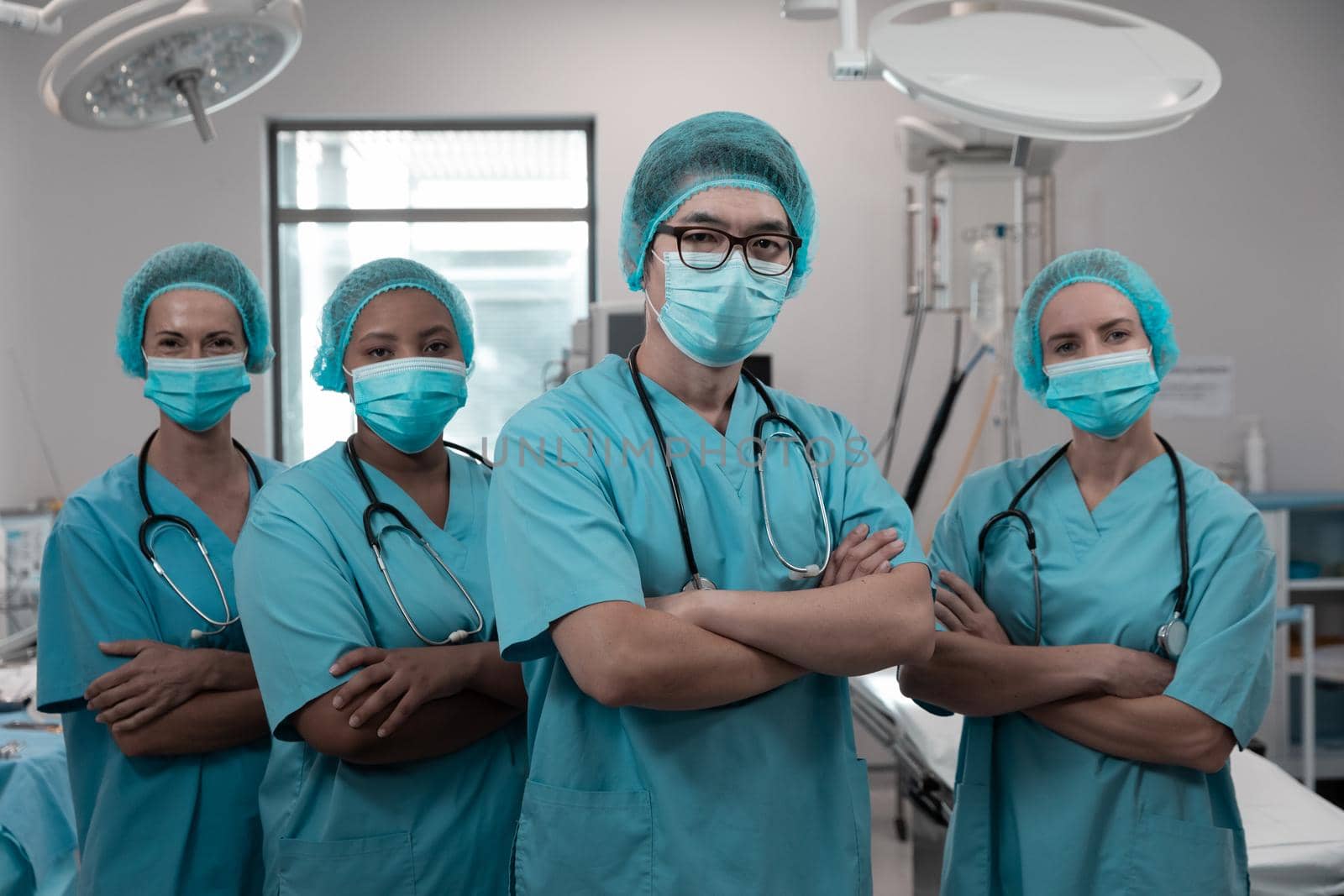 Diverse group of male and female doctors standing in operating theatre wearing face masks. medicine, health and healthcare services during coronavirus covid 19 pandemic.