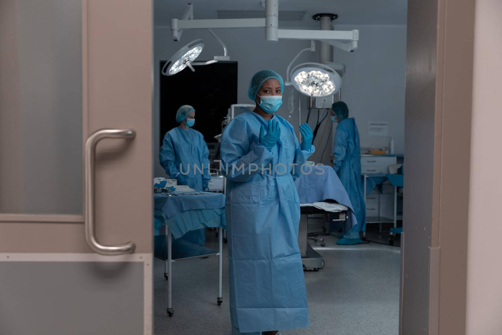 Diverse group of male and female doctors in operating theatre wearing face masks performing surgery. medicine, health and healthcare services during coronavirus covid 19 pandemic.