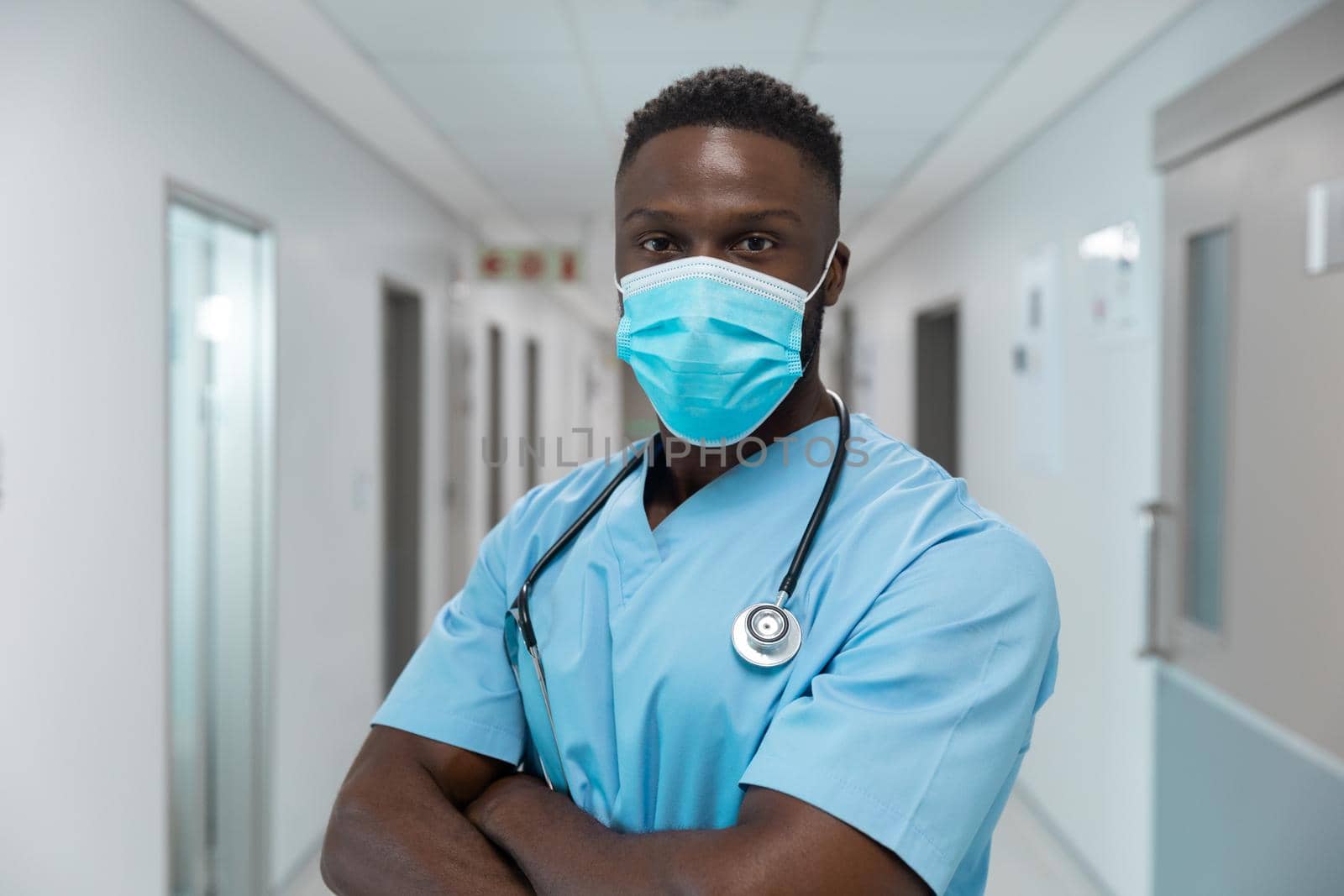 Portrait of african american male doctor wearing face mask standing in hospital corridor. medicine, health and healthcare services during coronavirus covid 19 pandemic.