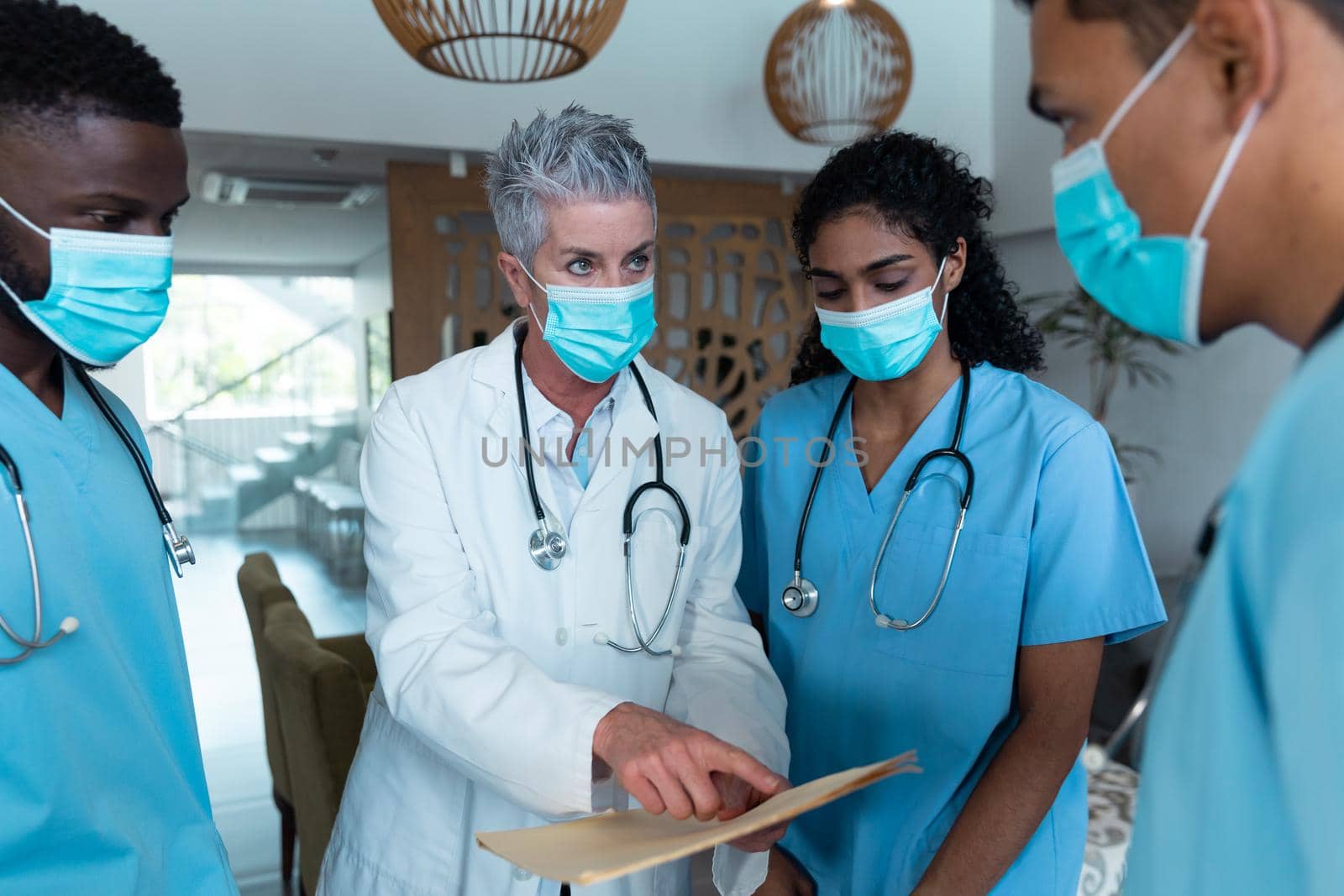 Caucasian female senior doctor and diverse hospital colleagues wearing face masks talking at meeting. medicine, health and healthcare services during covid 19 coronavirus pandemic.