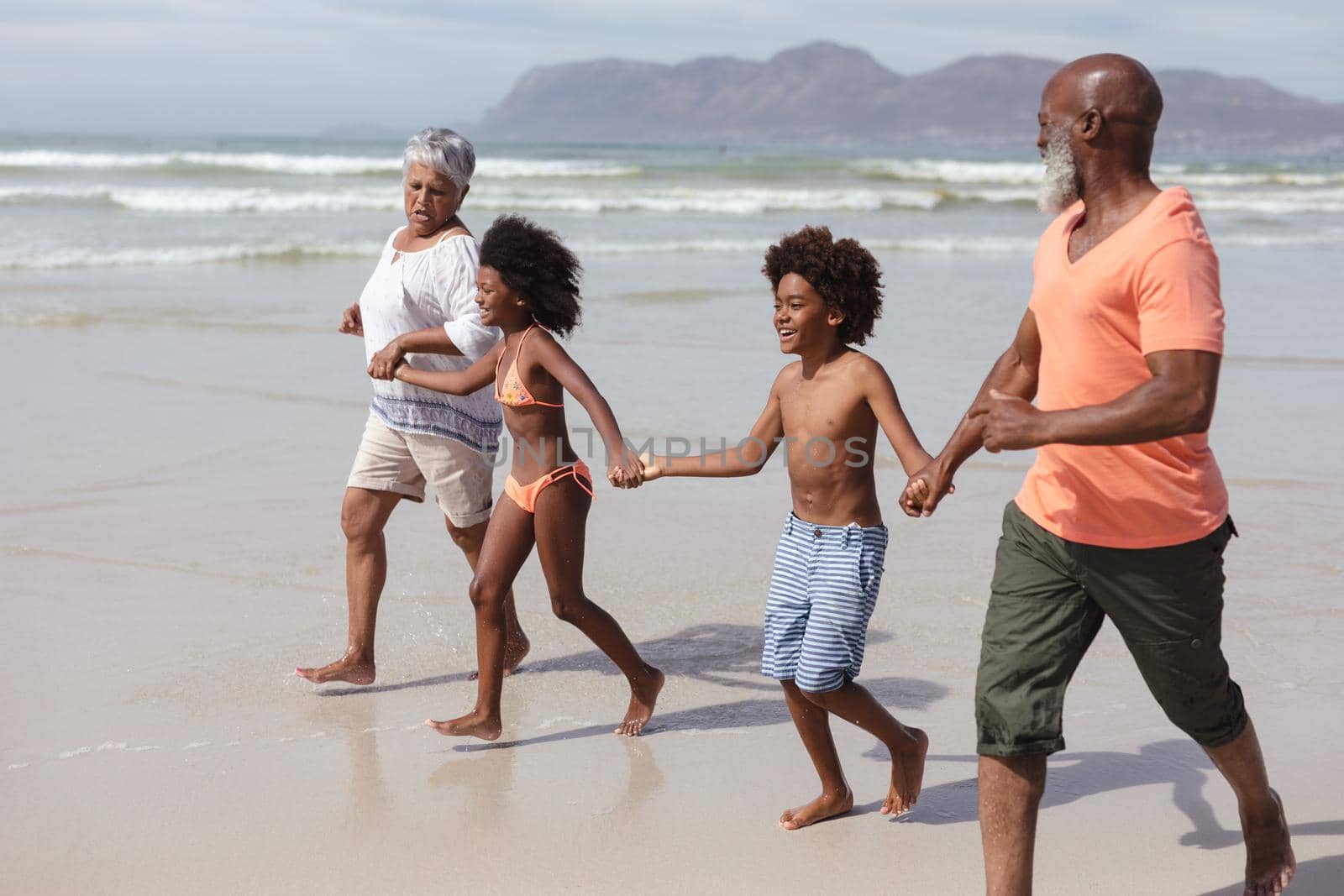 African american grandparents and grandchildren holding hands walking on the beach by Wavebreakmedia