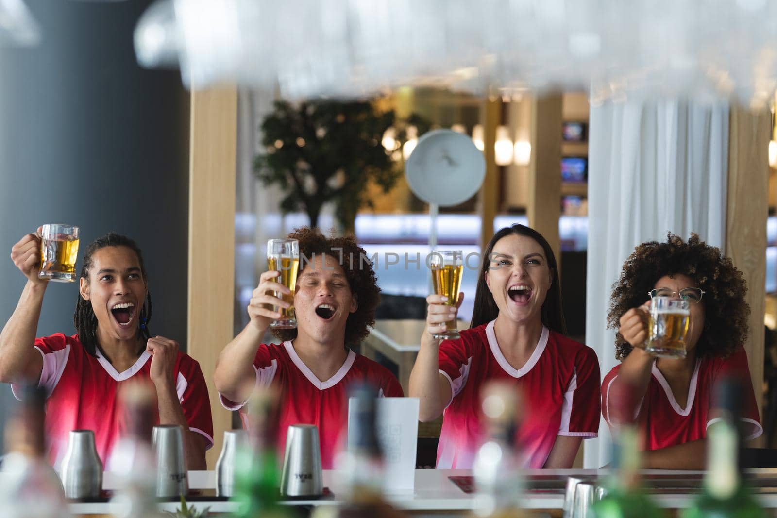 Diverse group of male and female sports fans raising glasses and watching game at bar. sports fan friends socialising and drinking at bar.