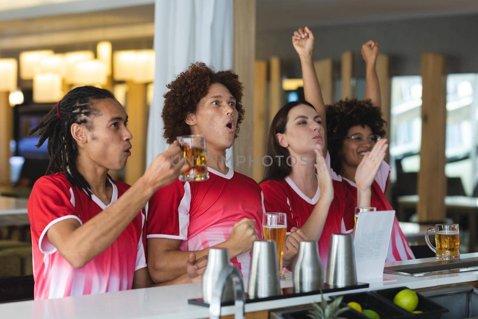 Diverse group of male and female sports fans raising glasses and watching game at bar. sports fan friends socialising and drinking at bar.
