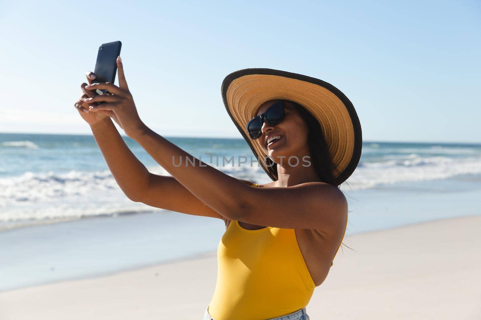 Smiling mixed race woman on beach holiday taking selfie. outdoor leisure vacation time by the sea.