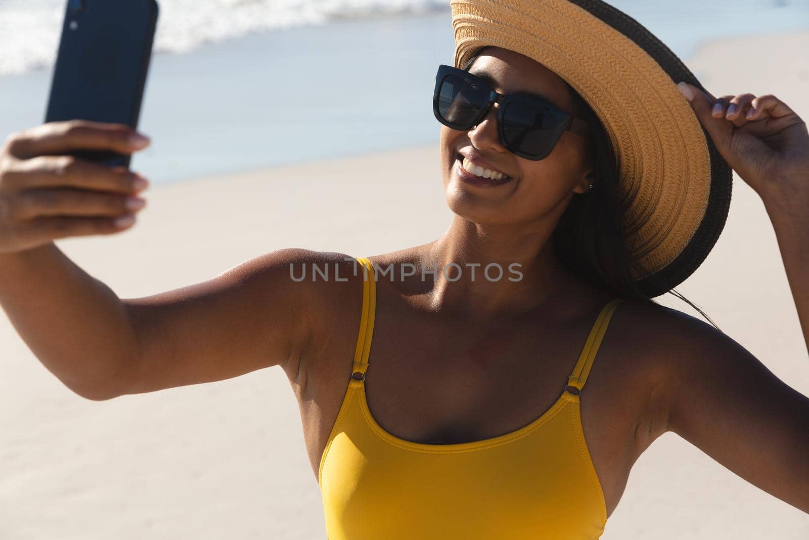 Smiling mixed race woman on beach holiday taking selfie. outdoor leisure vacation time by the sea.