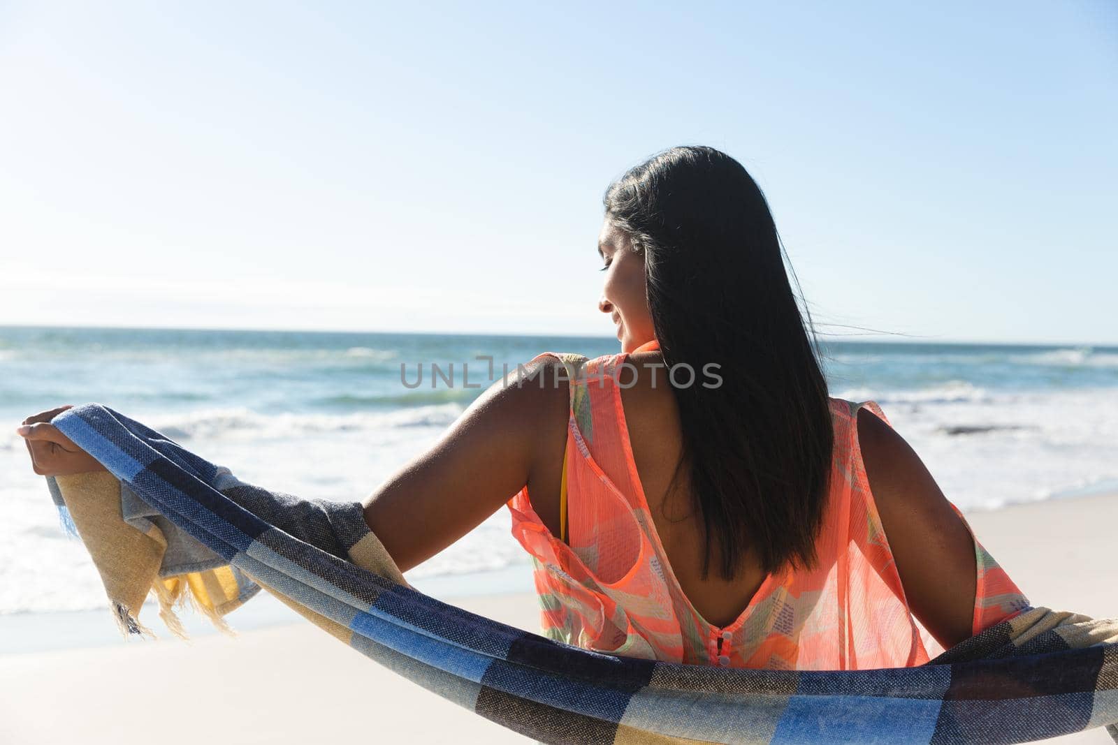 Smiling mixed race woman on beach holiday wearing shawl. outdoor leisure vacation time by the sea.