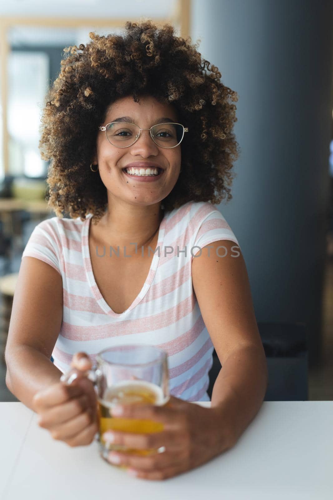 Portrait of mixed race woman sitting at table smiling having beer by Wavebreakmedia