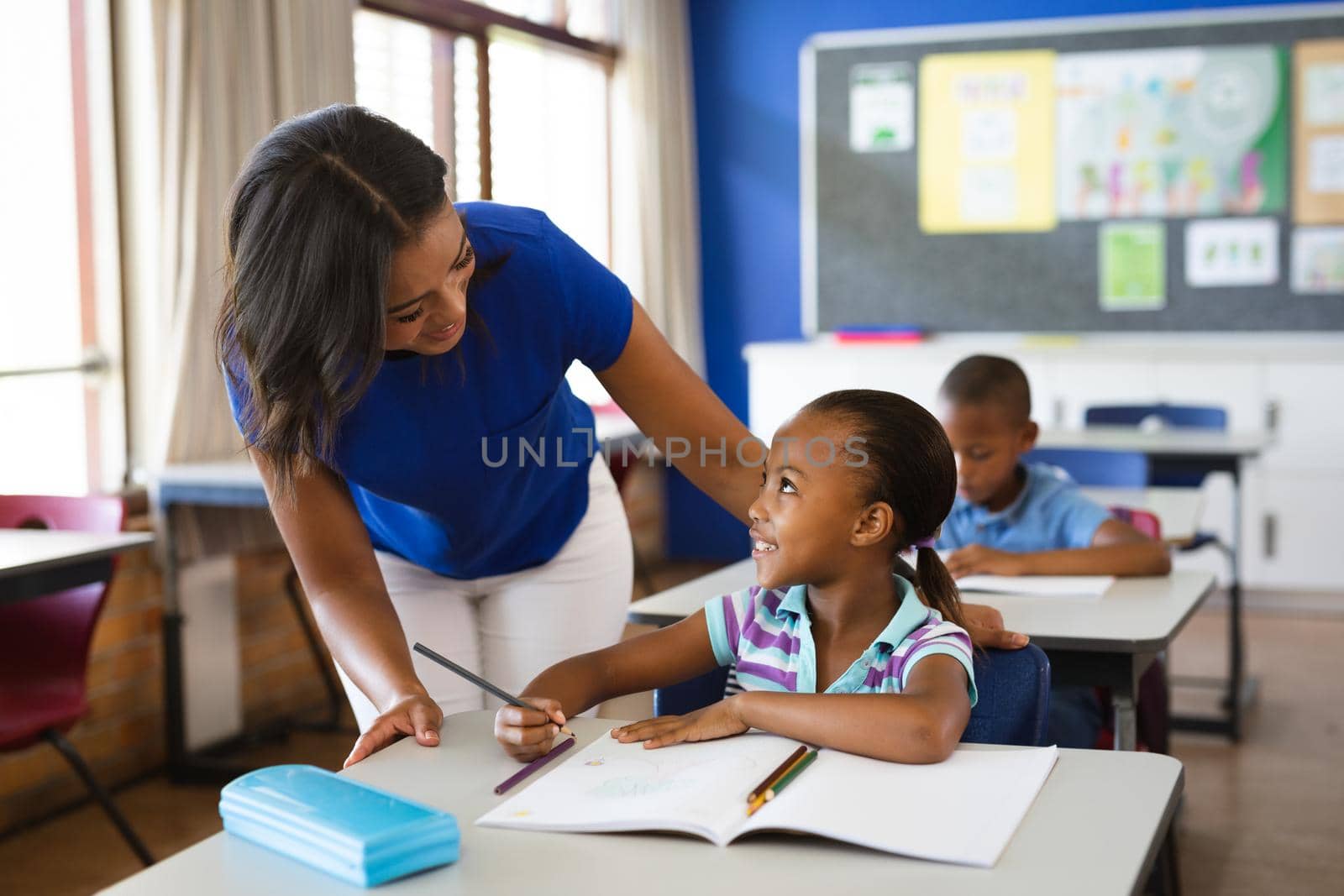 African american female teacher teaching african american girl in the class at elementary school. school and education concept