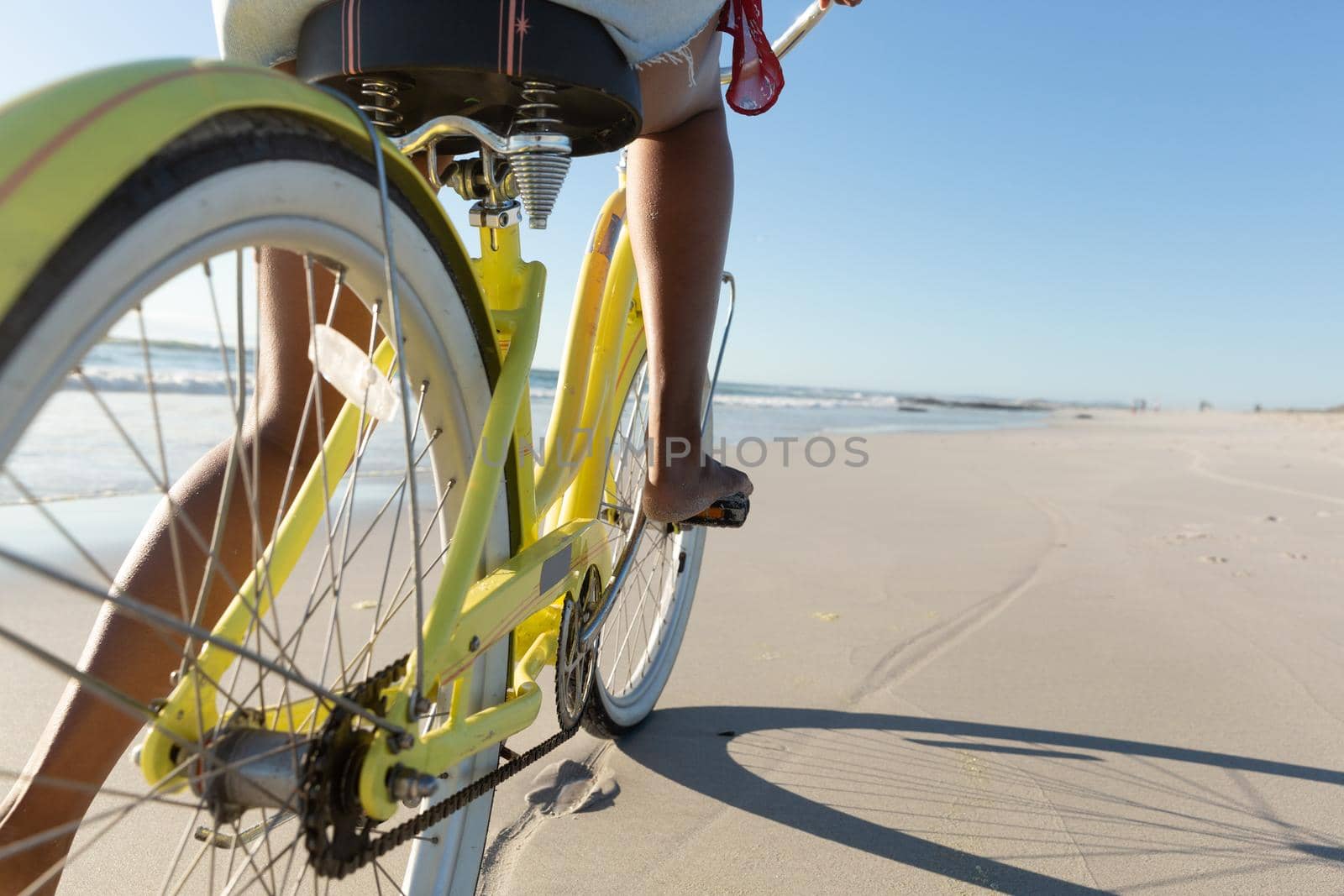 Low section of mixed race woman on beach holiday riding bicycle on the sand by the sea. outdoor leisure vacation time by the sea.