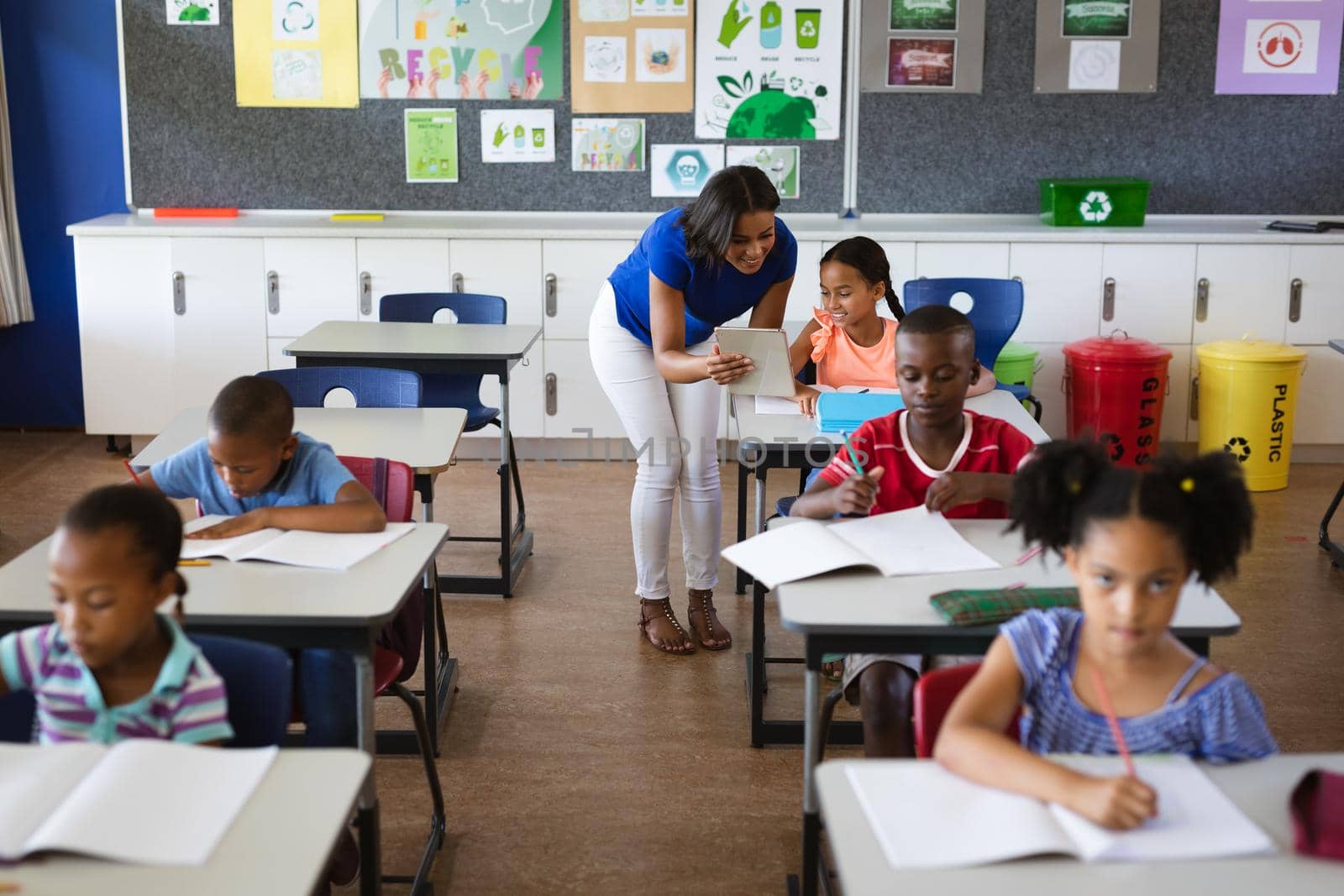 African american female teacher with digital tablet teaching a girl at elementary school. school and education concept