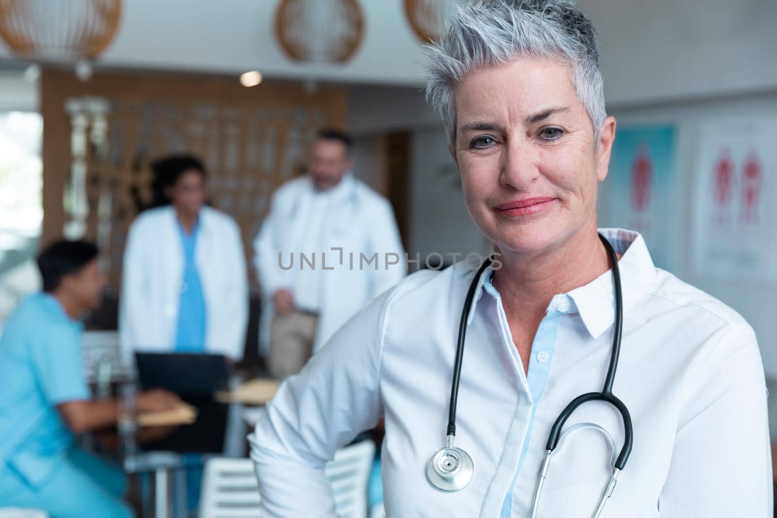 Portrait of smiling caucasian female senior doctor, with colleagues in discussion in the background. medicine, health and healthcare services.