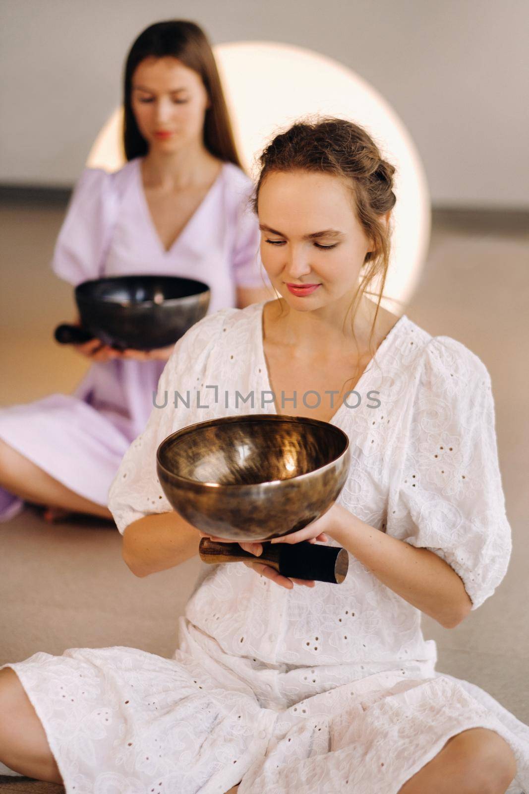 Two female yoga teachers playing a Tibetan bowl in the gym during a yoga retreat.