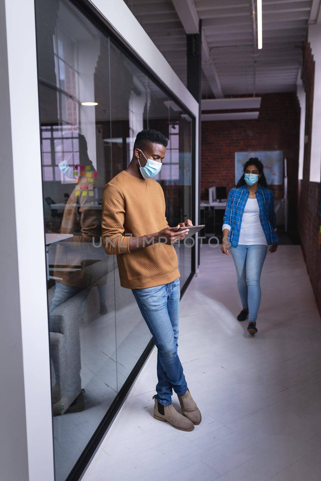 Diverse male and female colleagues wearing face mask standing in corridor. independent creative design business during covid 19 coronavirus pandemic.