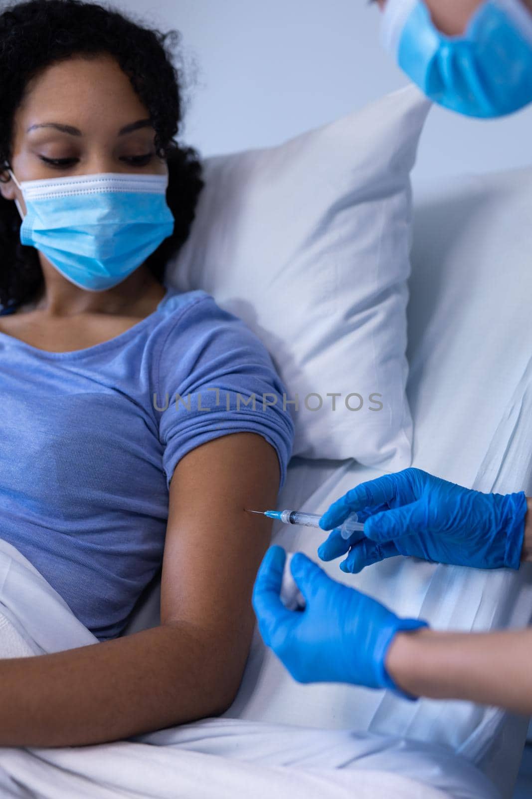 Caucasian female doctor in hospital wearing face mask vaccinating african american female patient. medical professional at work during coronavirus covid 19 pandemic.