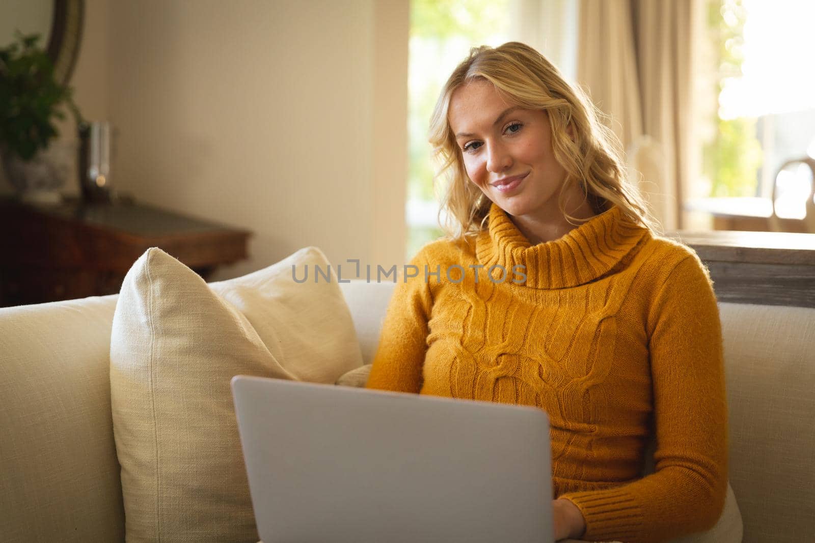Portrait of happy caucasian woman sitting on couch in living room using laptop, smiling. spending free time at home with technology.