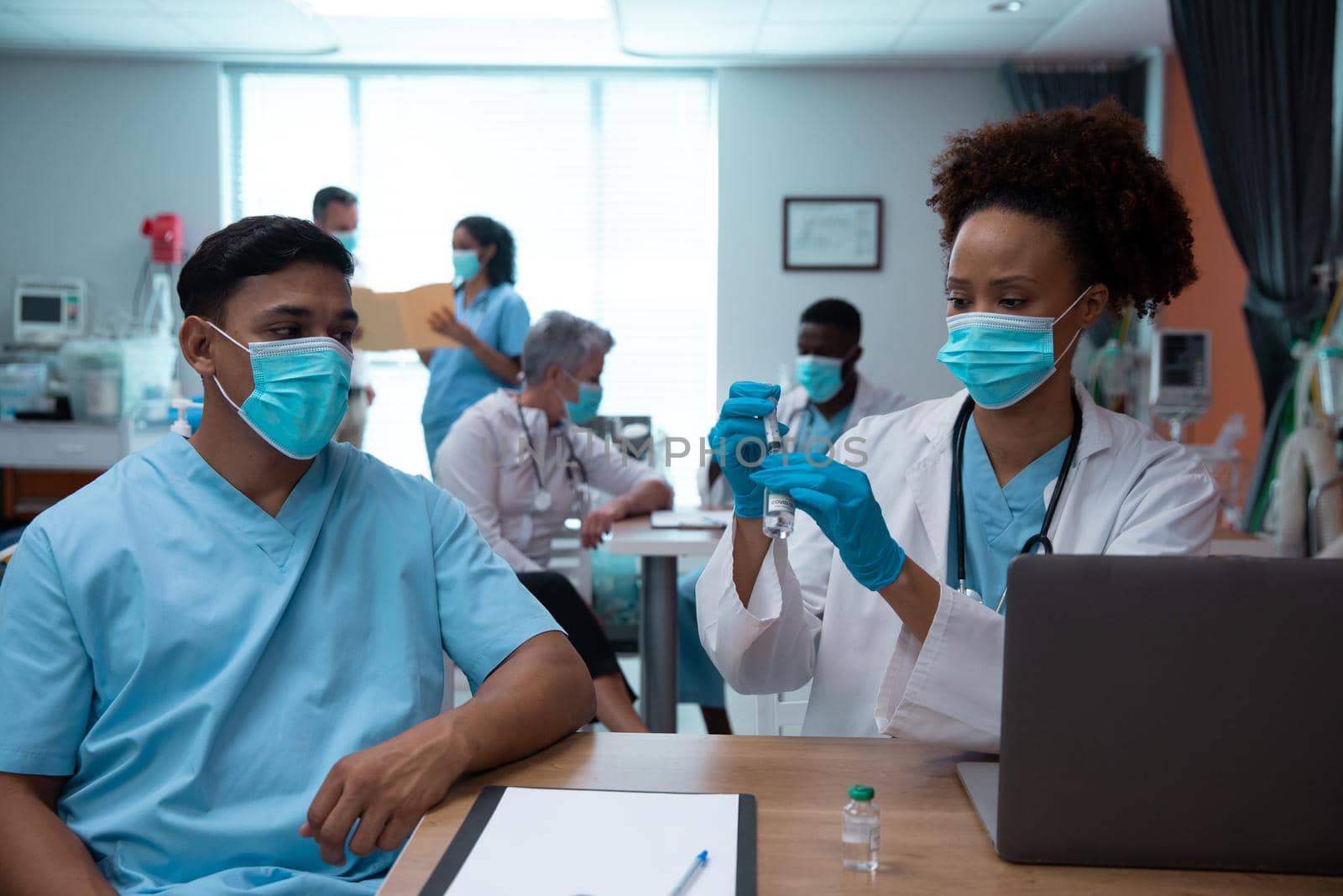 Mixed race couple of doctors wearing face masks preparing to make injection. medicine, health and healthcare services during coronavirus covid 19 pandemic.