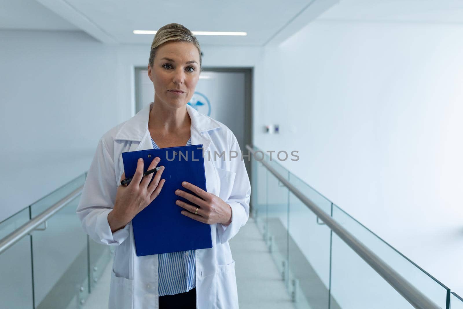 Portrait of caucasian female doctor standing in hospital corridor holding medical chart document by Wavebreakmedia