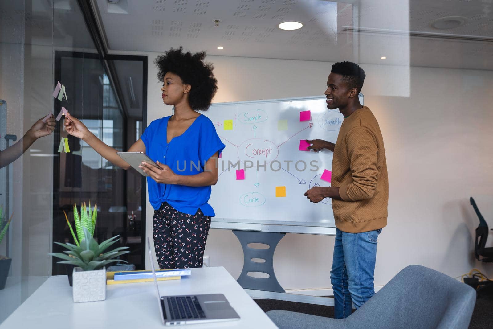 Diverse male and female colleagues sticking memo notes on glass wall and whiteboard in background. independent creative design business.