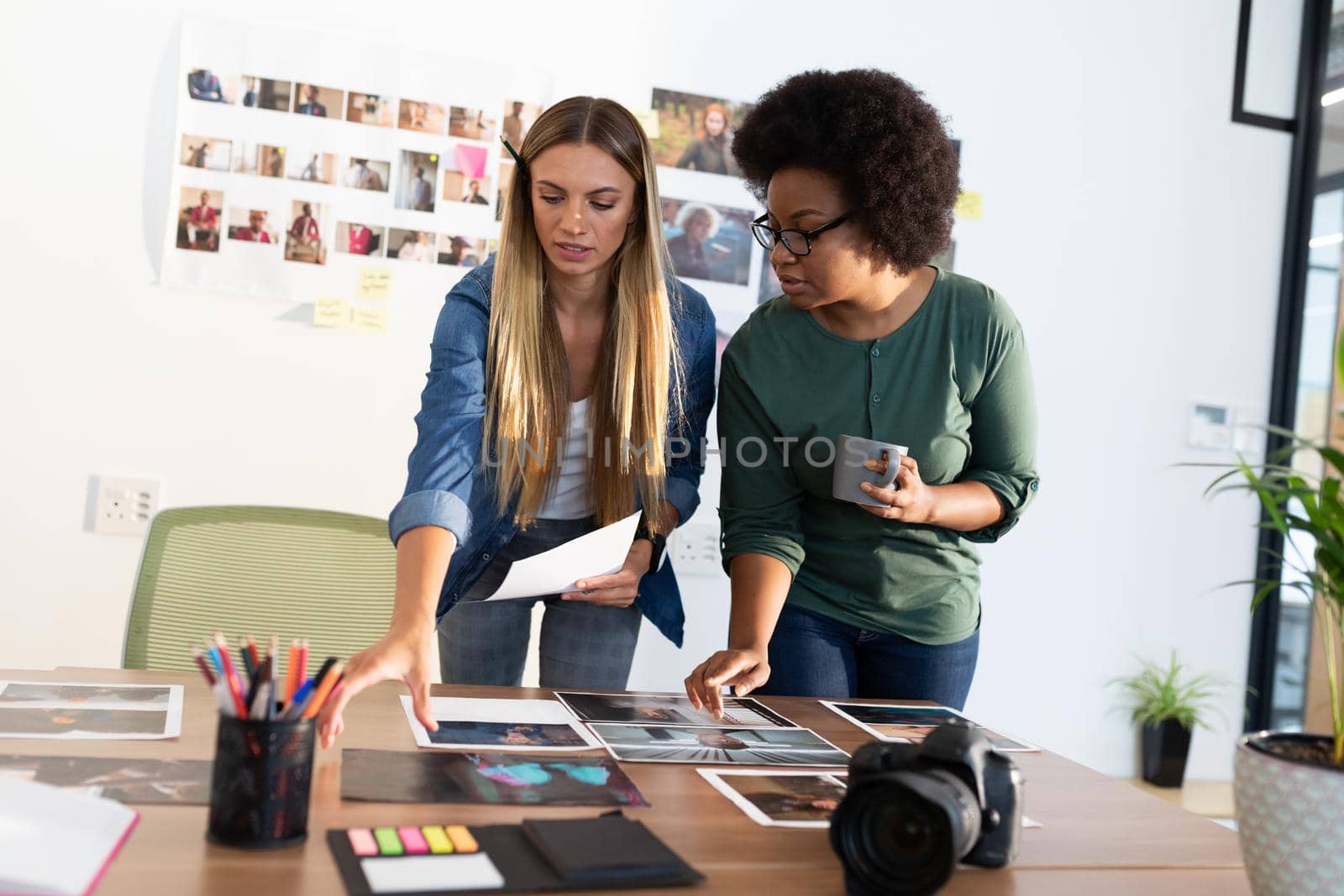 Diverse female business colleagues brainstorming looking at photos in meeting room by Wavebreakmedia