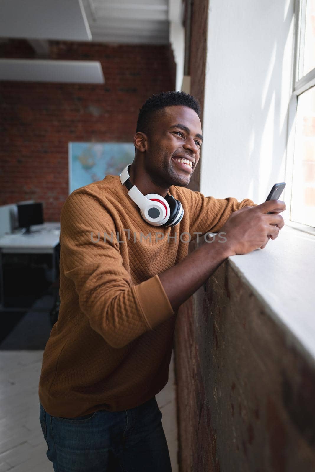 African american businessman standing in office with head phones off having video call on smartphone by Wavebreakmedia