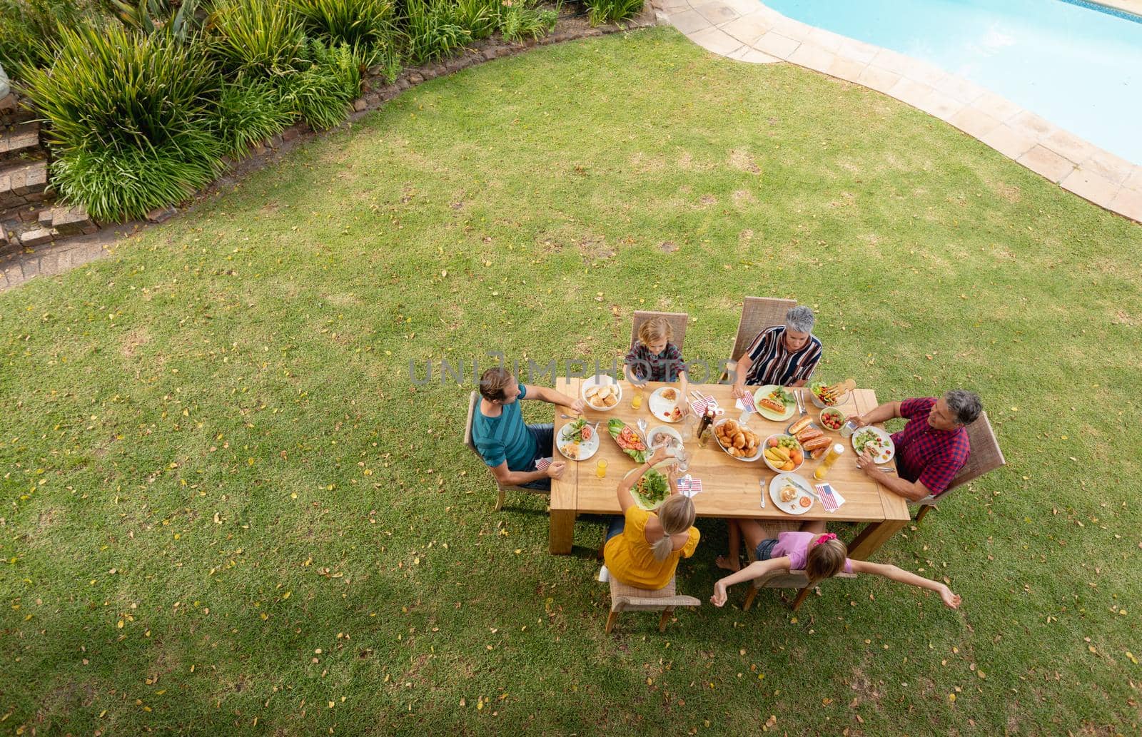 High angle view of caucasian three generation family sitting at table eating meal in garden by Wavebreakmedia