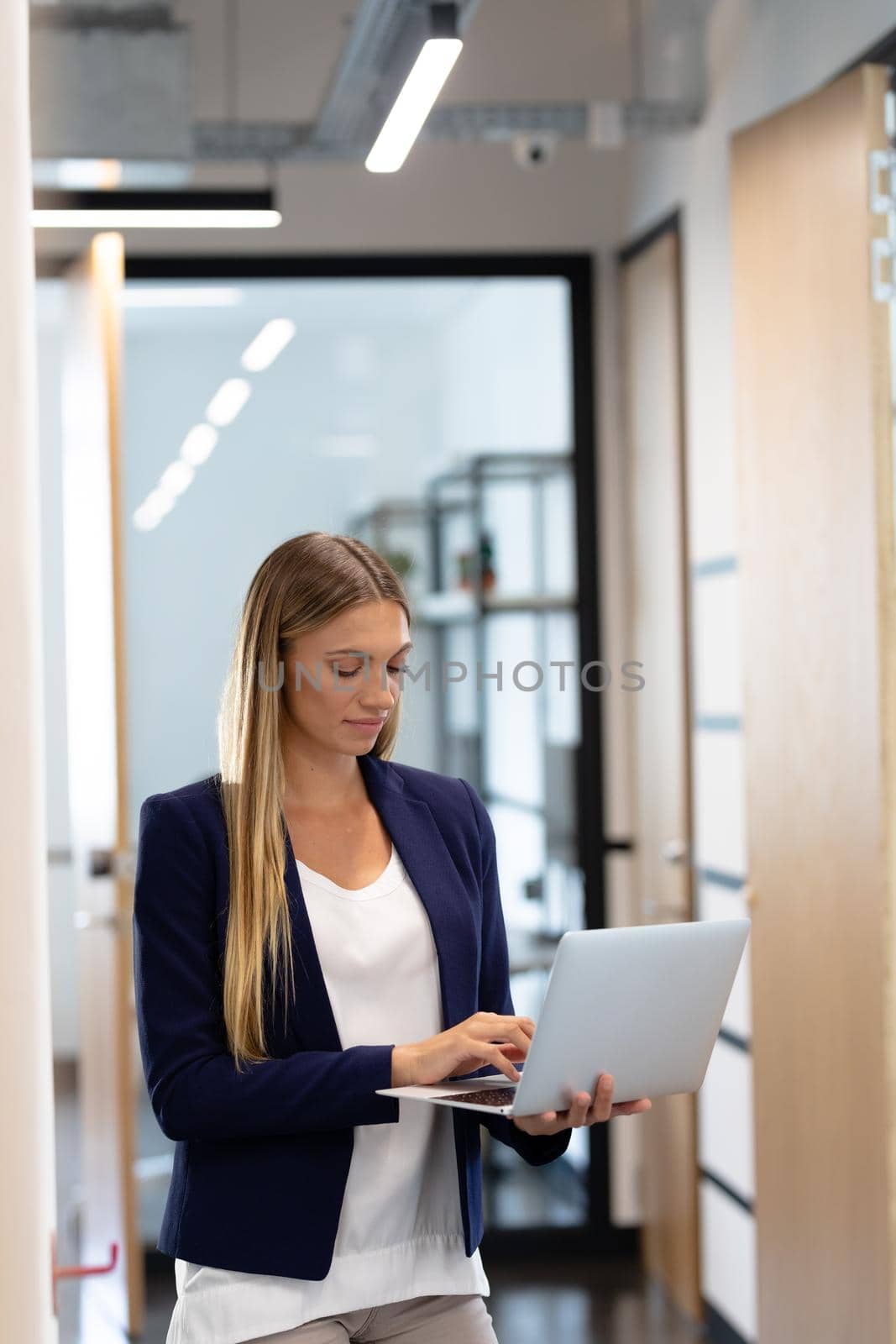 Smartly dressed caucasian businesswoman standing in corridor using laptop computer. business in a modern office.