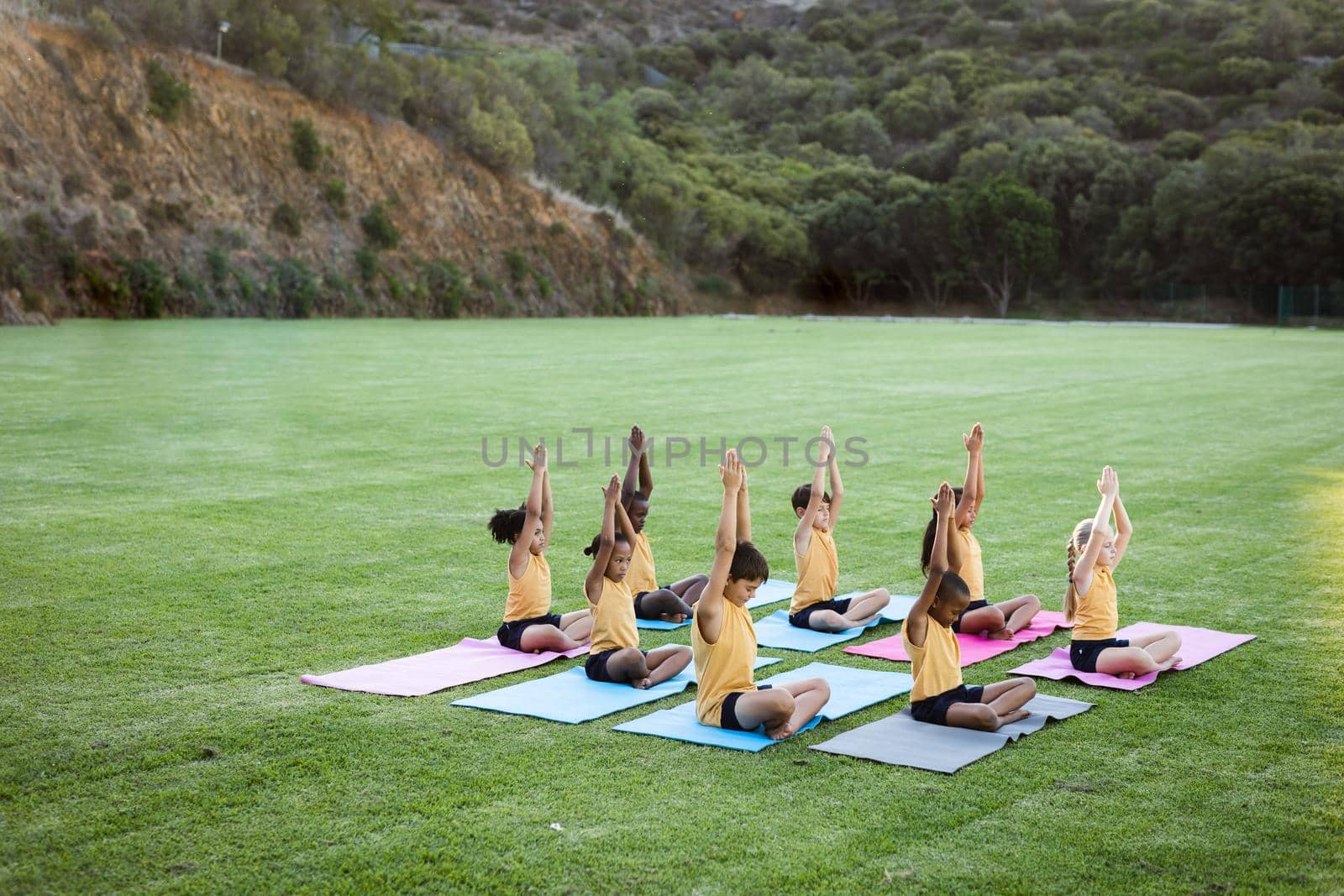 Group of students practicing yoga and meditating sitting on yoga mat in garden at elementary school by Wavebreakmedia