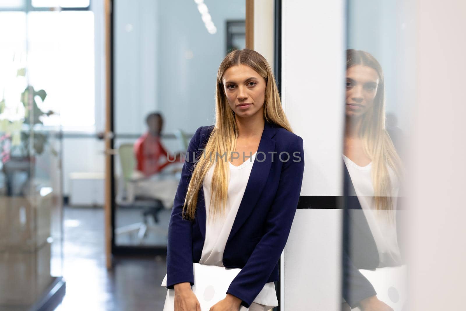 Caucasian businesswoman standing in corridor holding laptop looking to camera. business in a modern office.