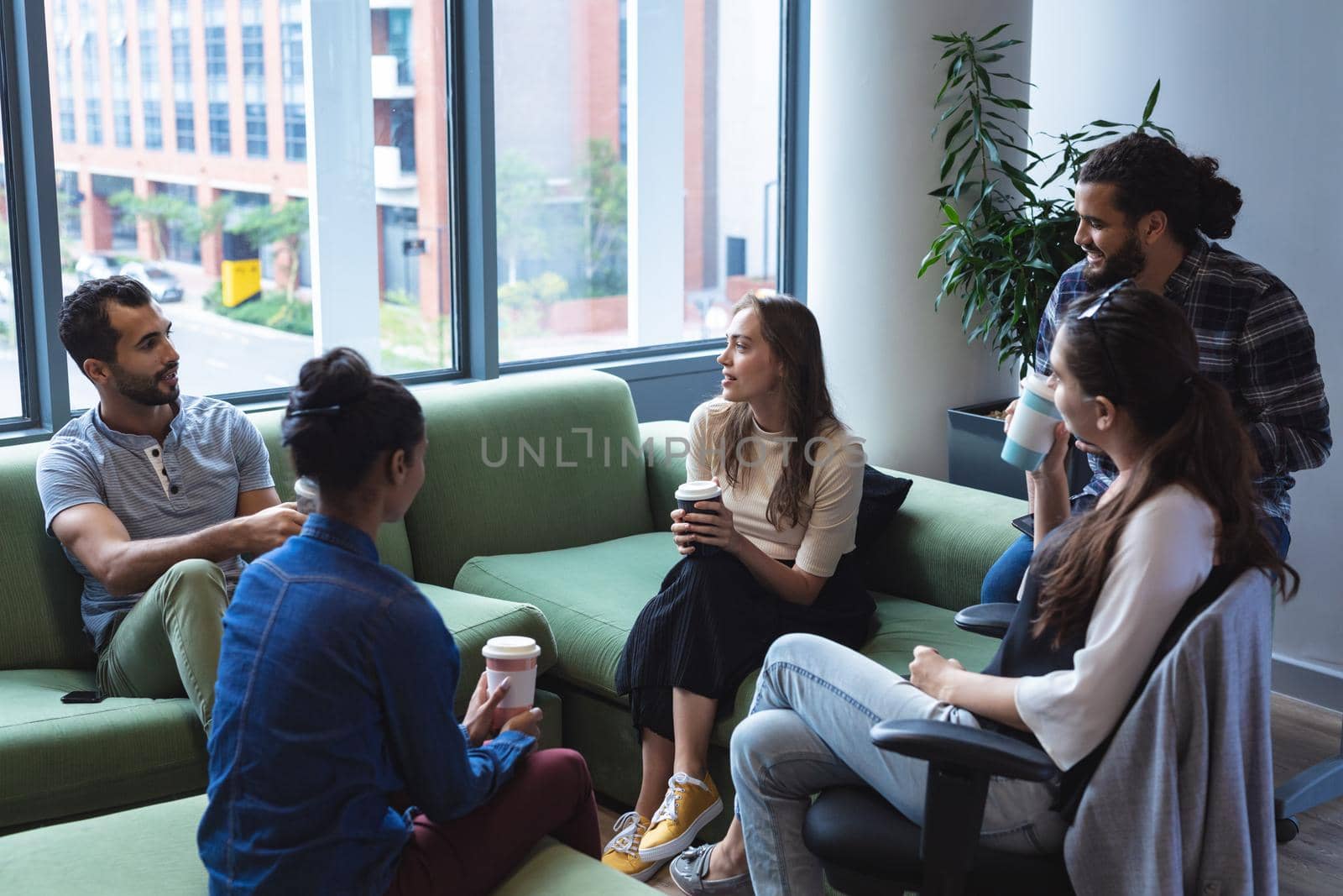 Diverse group of creative colleagues holding takeaway coffees, talking at casual meeting. modern office of a creative design business.