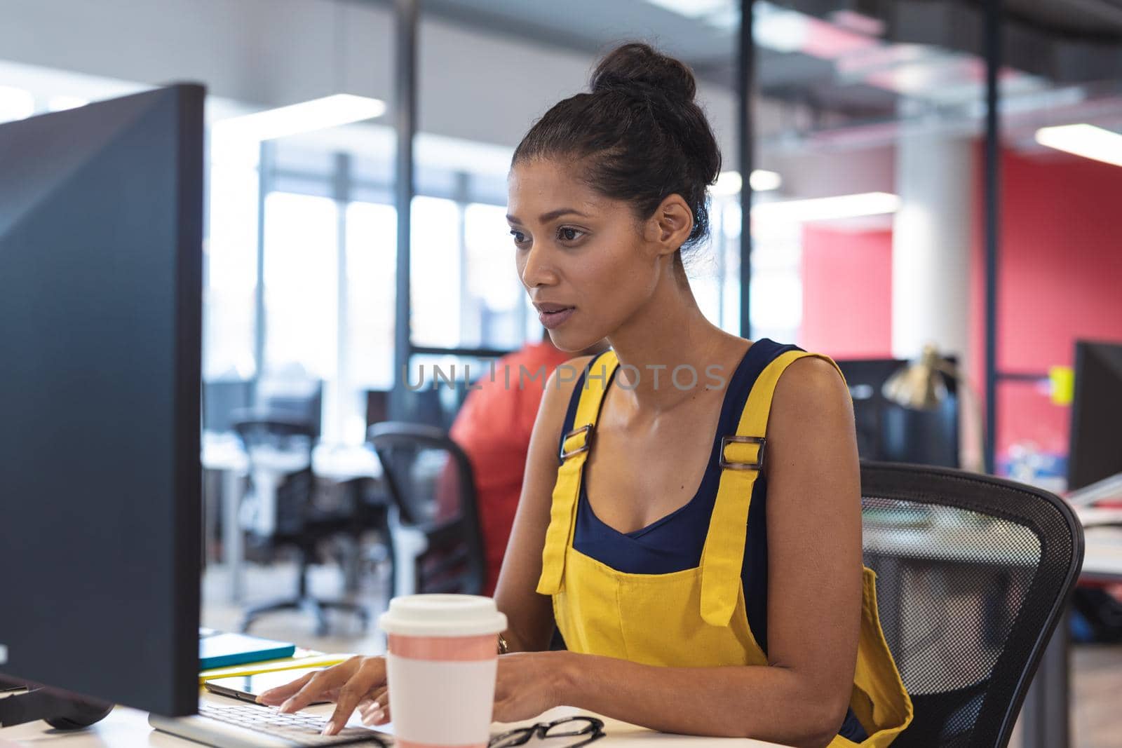 Mixed race female creative worker sitting at desk using computer. modern office of a creative design business.