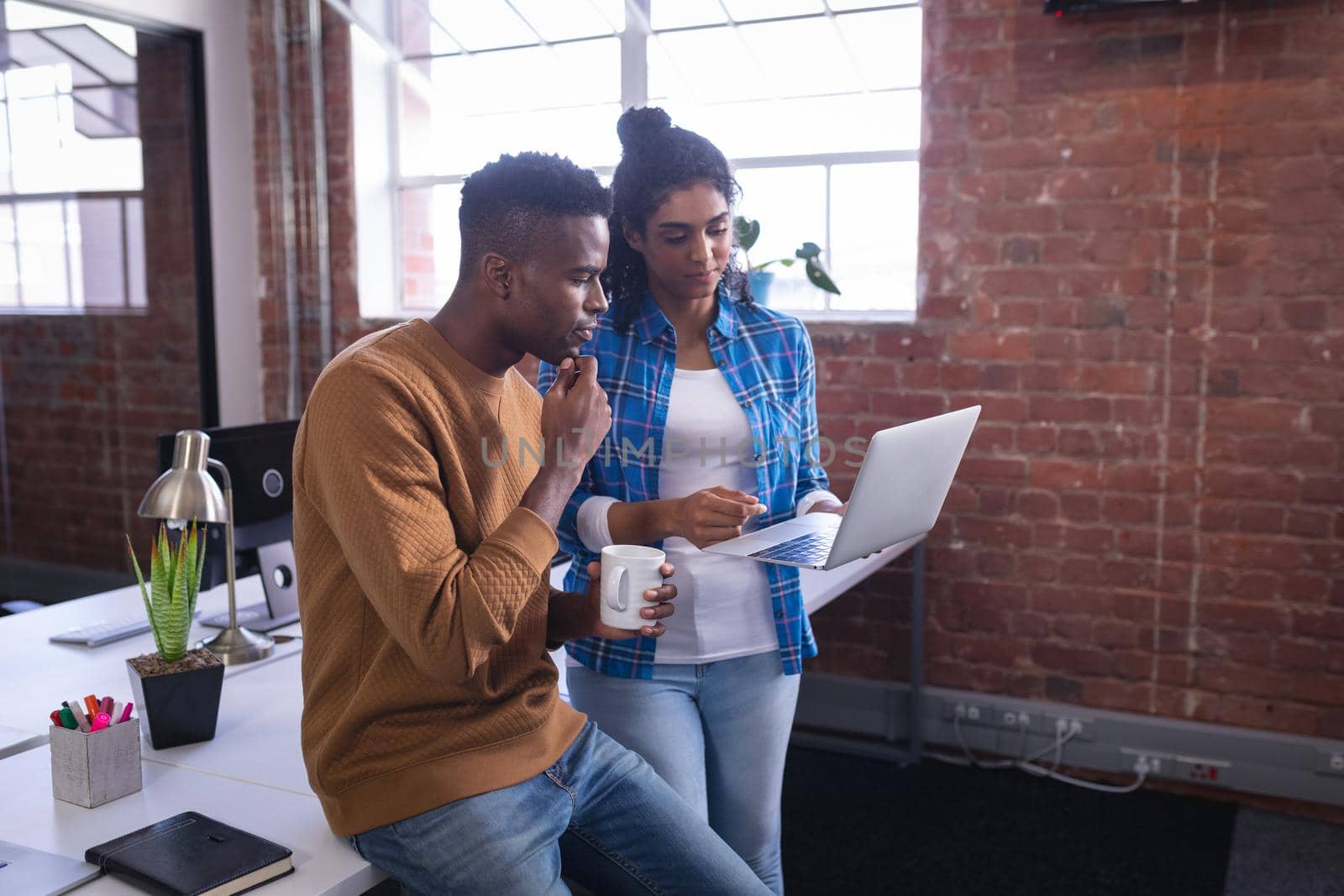 Diverse male and female colleagues at work standing discussing in front of laptop. independent creative design business.