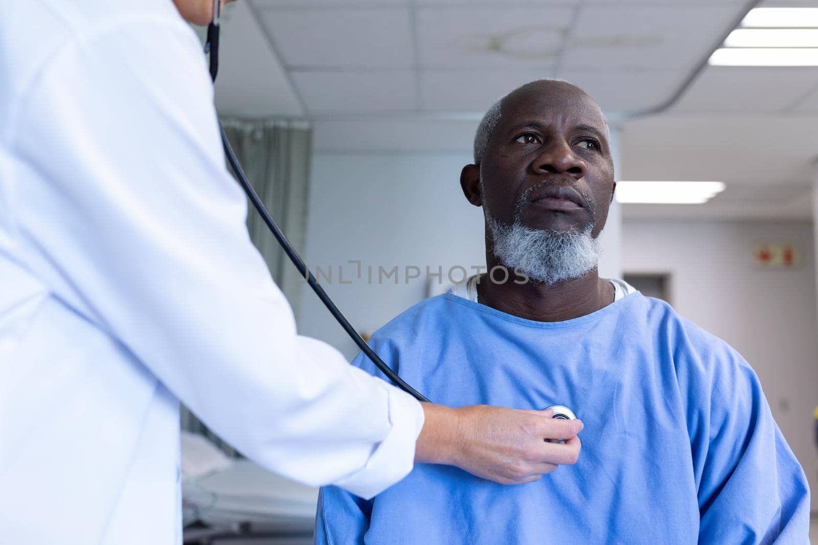 Caucasian female doctor examining with stethoscope african american male patient in hospital room by Wavebreakmedia