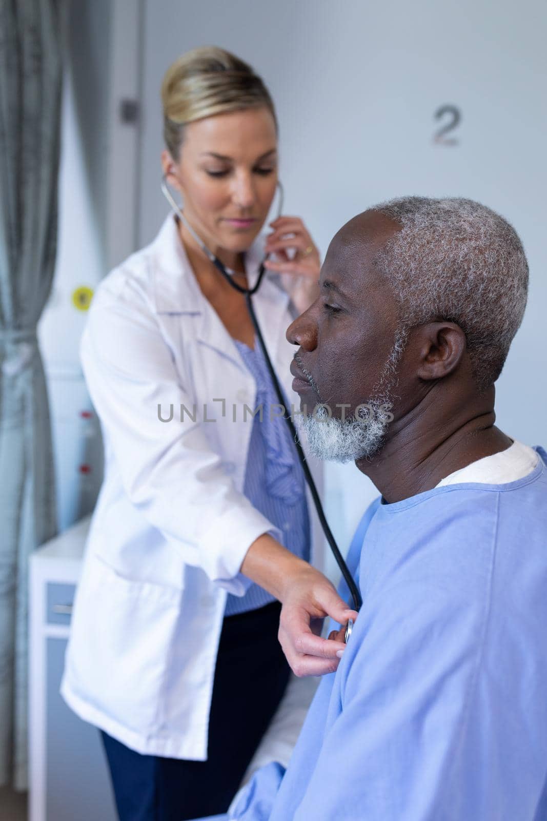 Caucasian female doctor examining with stethoscope african american male patient in hospital room by Wavebreakmedia