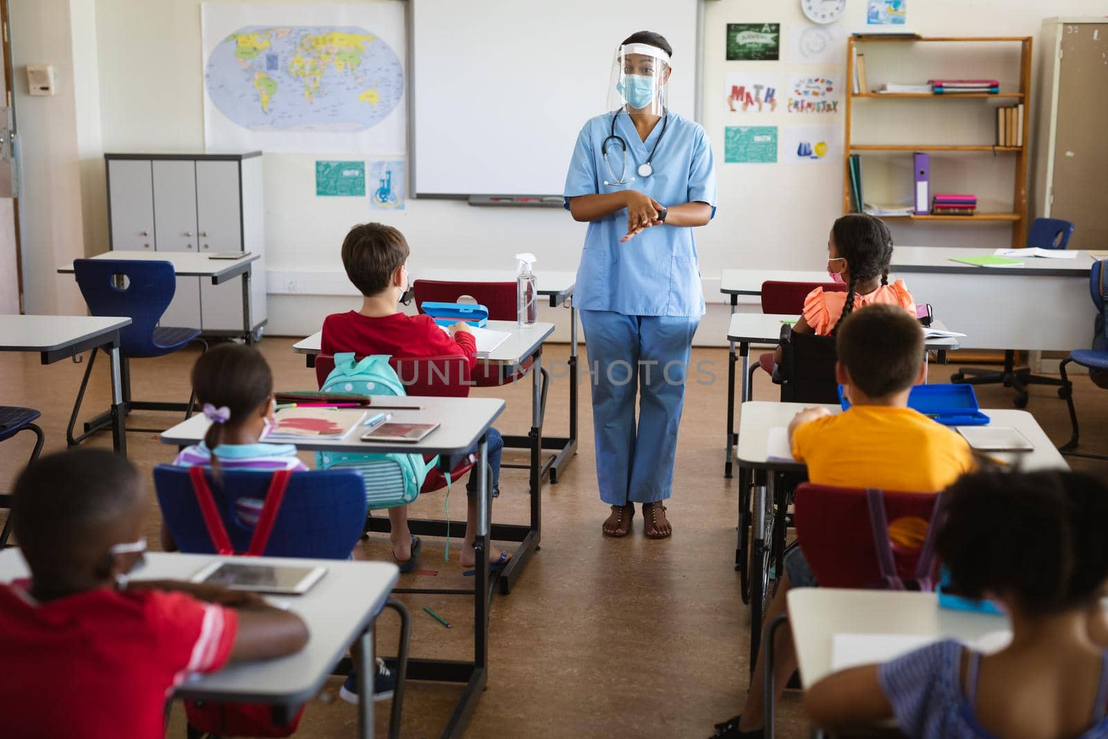Female health worker wearing face shield talking to students in the class at elementary school. education back to school health safety during covid19 coronavirus pandemic.