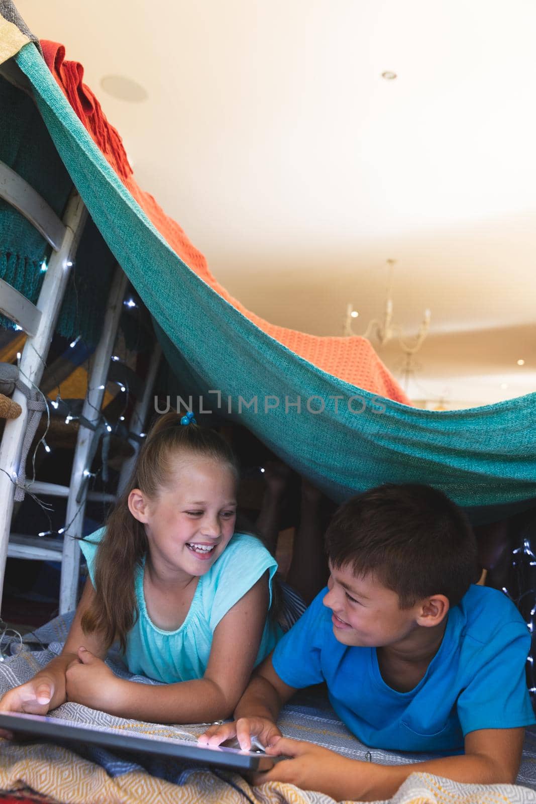 Caucasian brother and sister smiling, lying in blanket fort using tablet at home by Wavebreakmedia