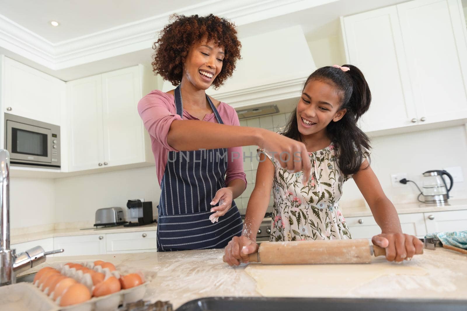 Happy african american mother with daughter baking in kitchen rolling dough by Wavebreakmedia