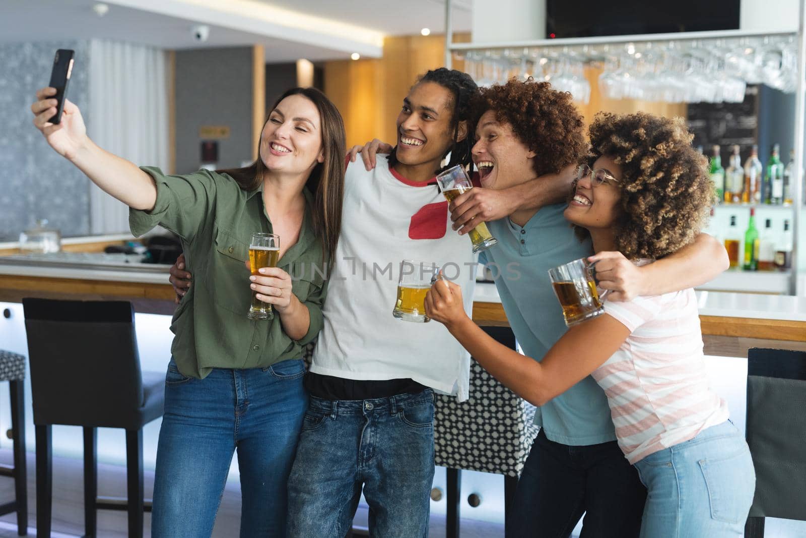 Diverse group of male and femalefriends raising glasses and taking selfie at bar. friends socialising and drinking at bar.