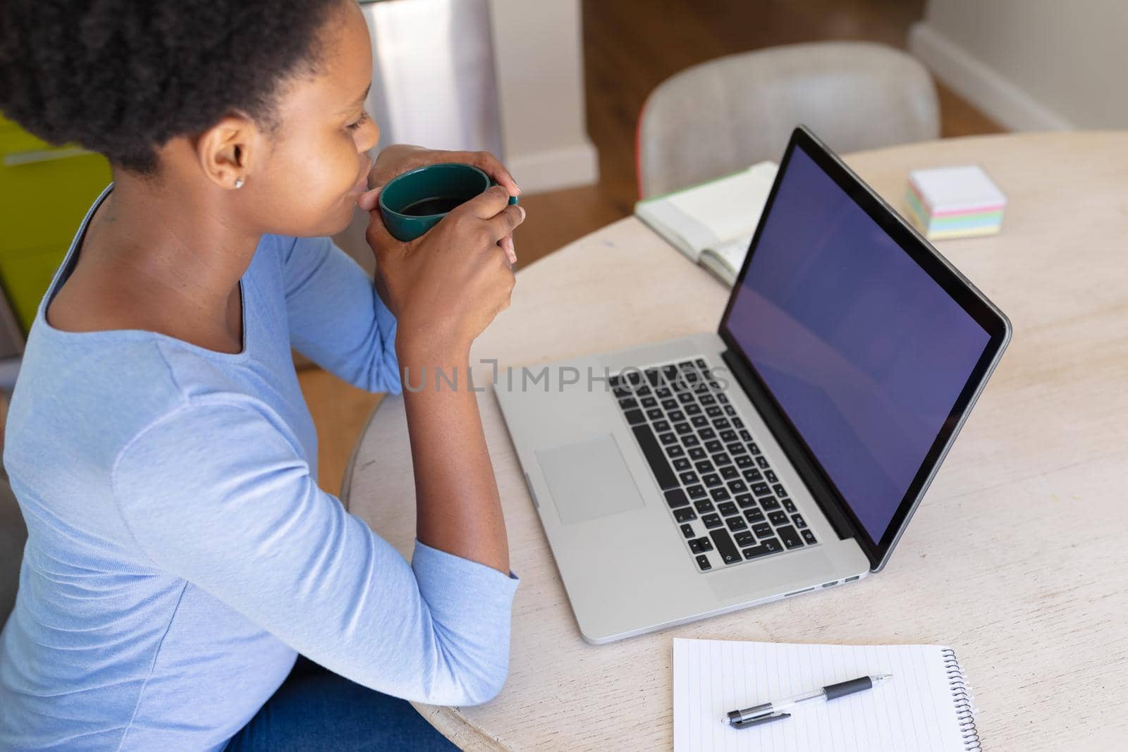 African american woman working from home, using laptop with copy space on screen, drinking coffee. staying at home in isolation during quarantine lockdown.